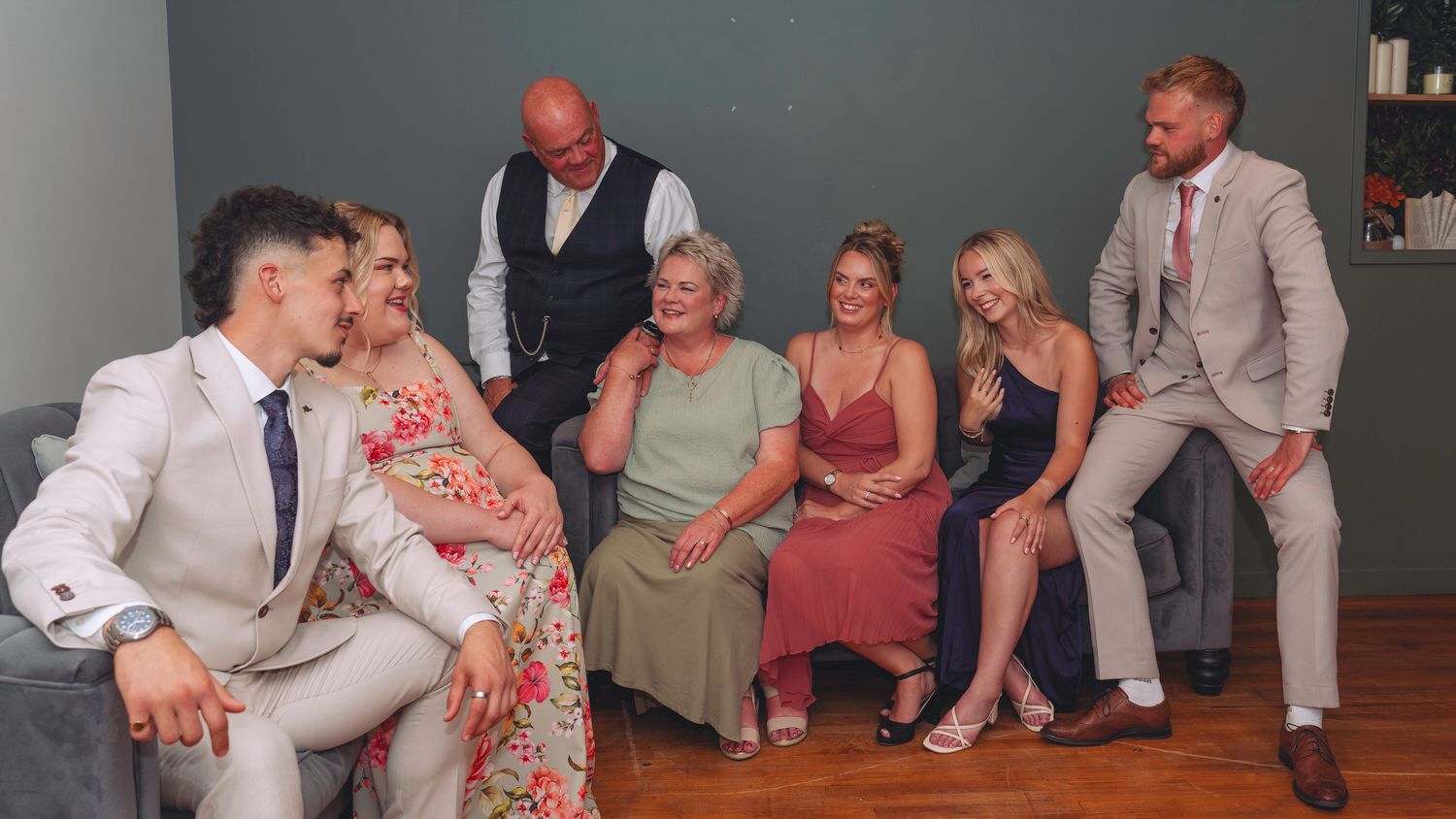 Group of seven people in formal attire posing together, smiling in a decorated indoor setting.