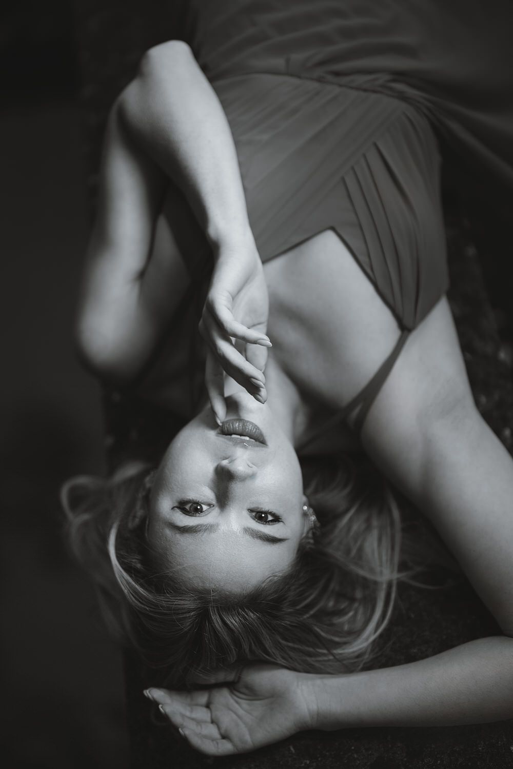 Black and white photo of a woman in a dress lying on the floor, looking up at the camera.