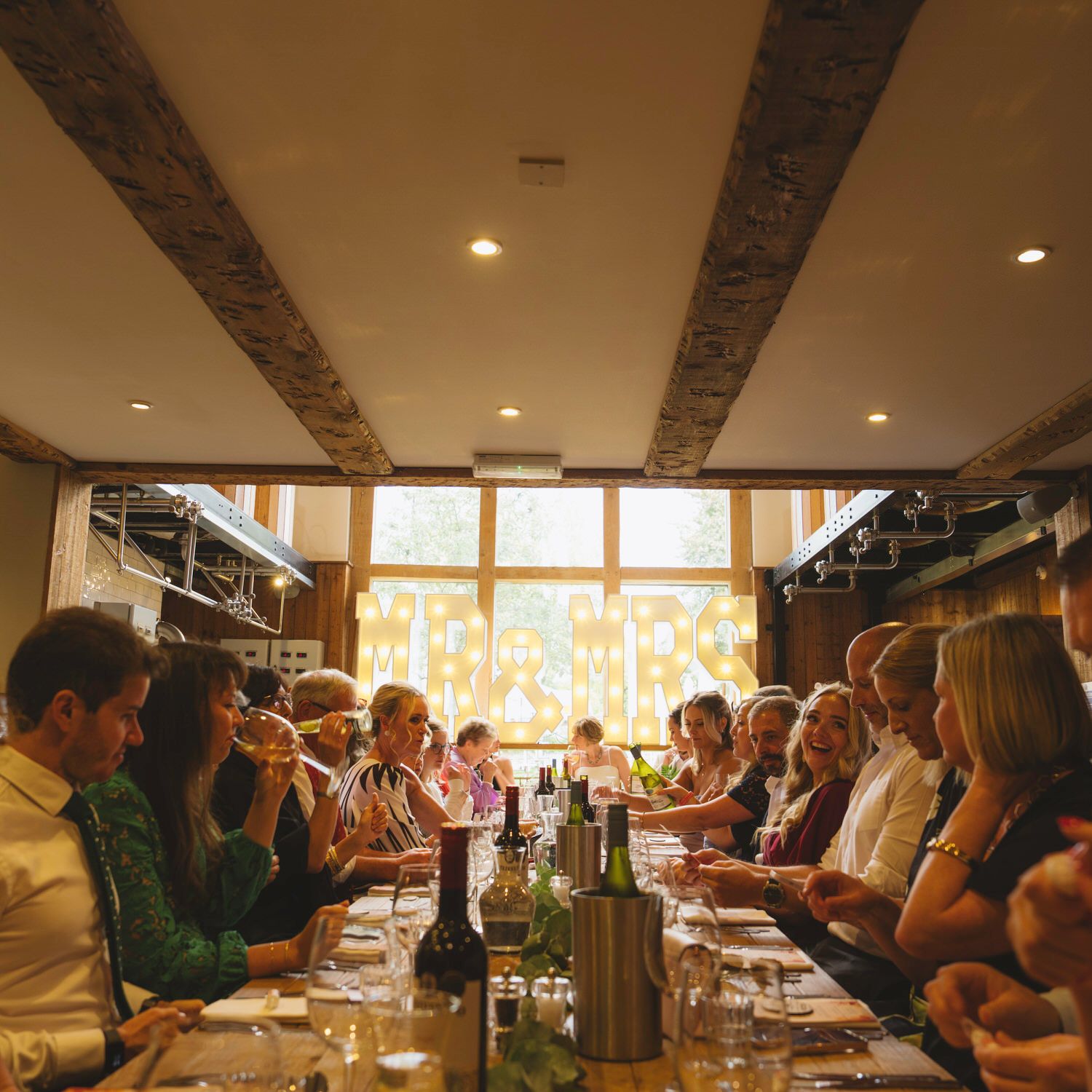 Guests dining at a long restaurant table in a warmly lit private dining room with large windows.