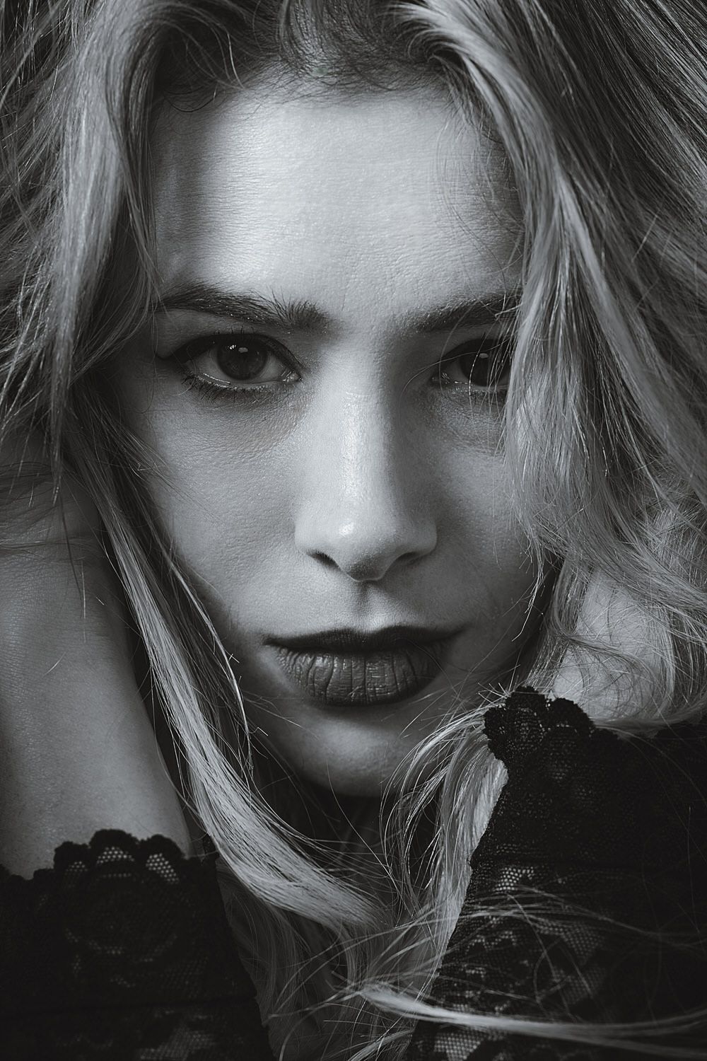 Black and white portrait of a blonde woman with dark lips and intense gaze wearing lace top.