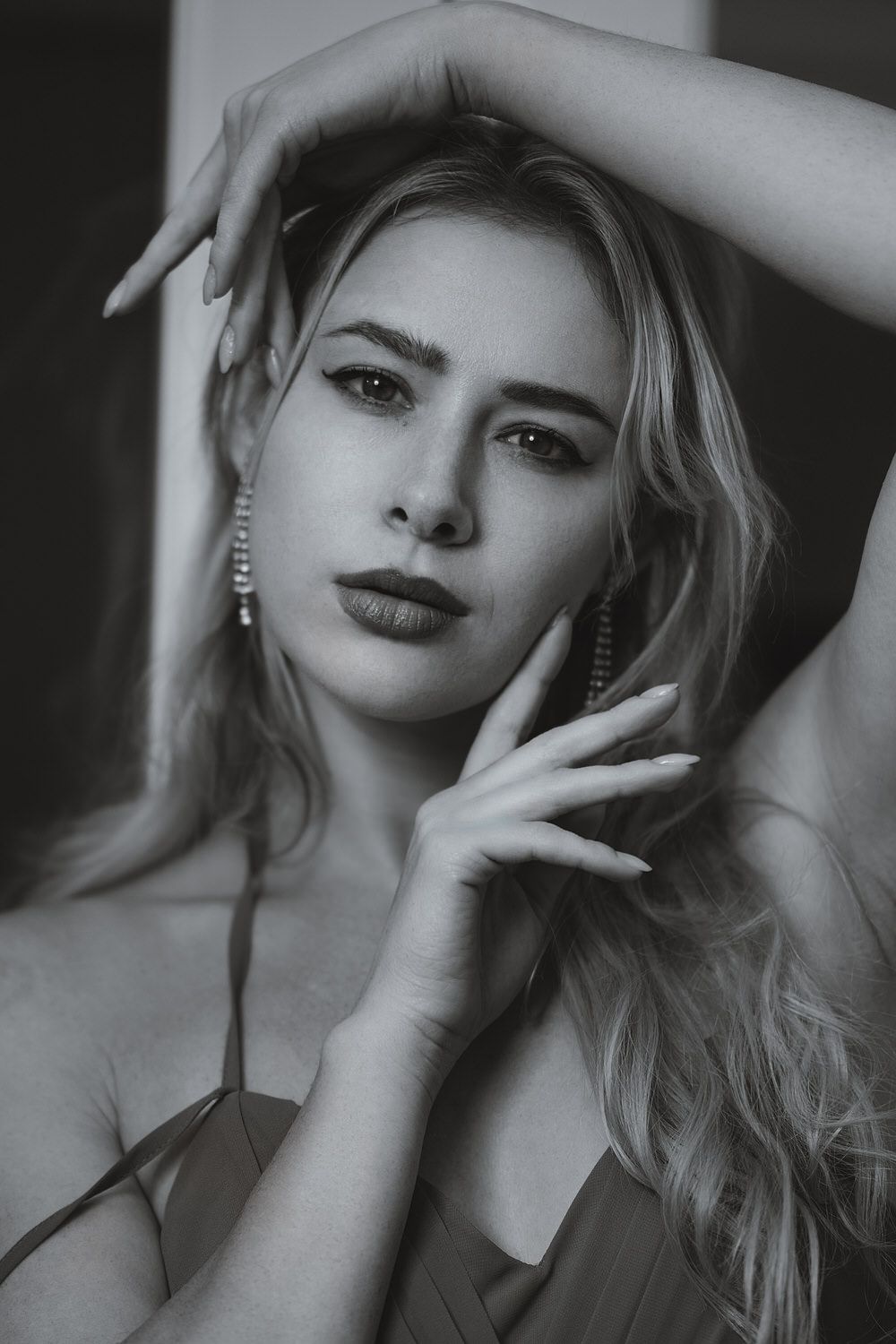 Black and white portrait of a blonde woman with dangling earrings, posing gracefully with hands near her face.