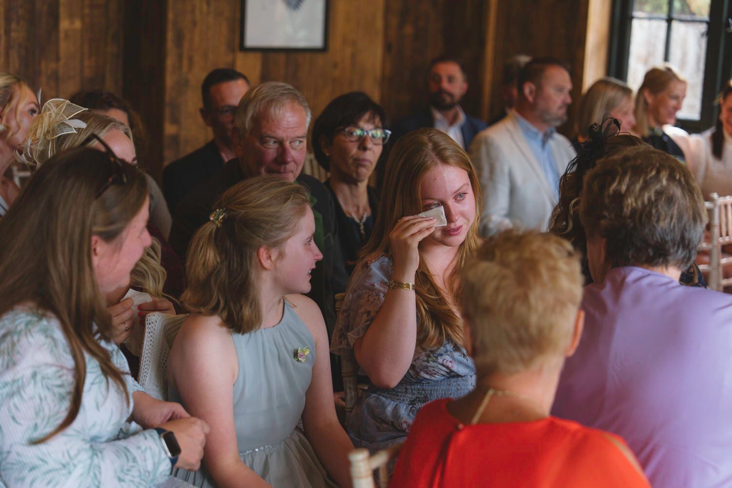 Emotional guests crying and consoling each other at an indoor wedding reception in a rustic venue.