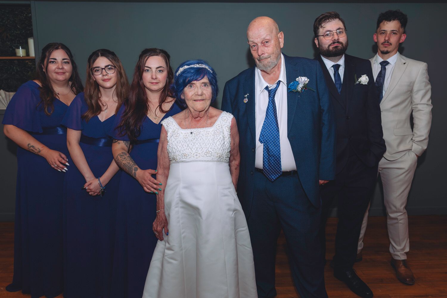 Wedding group photo with bride in white, groom in blue suit, and family members in coordinating blue attire.