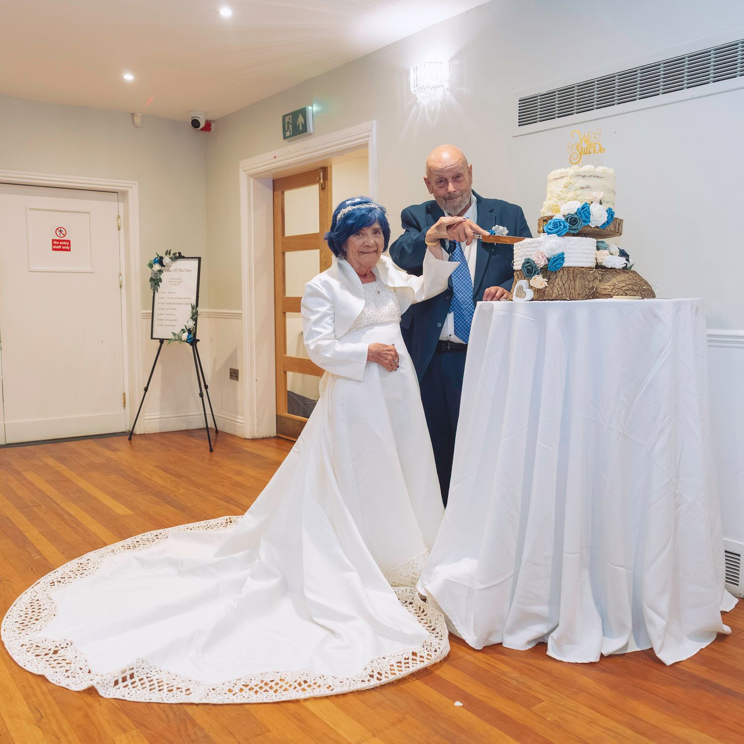 Bride and groom cutting their wedding cake at a reception venue, bride wearing elegant white gown with lace trim.