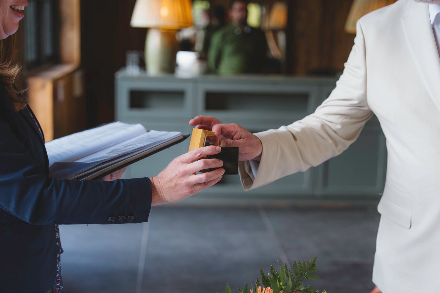 Two people exchanging a small gift or card at a formal indoor event, one holding a binder.
