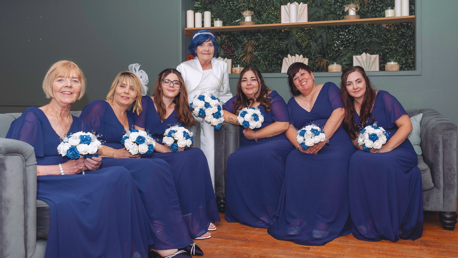 Bride in white gown with six bridesmaids in navy blue dresses holding blue and white bouquets at wedding.