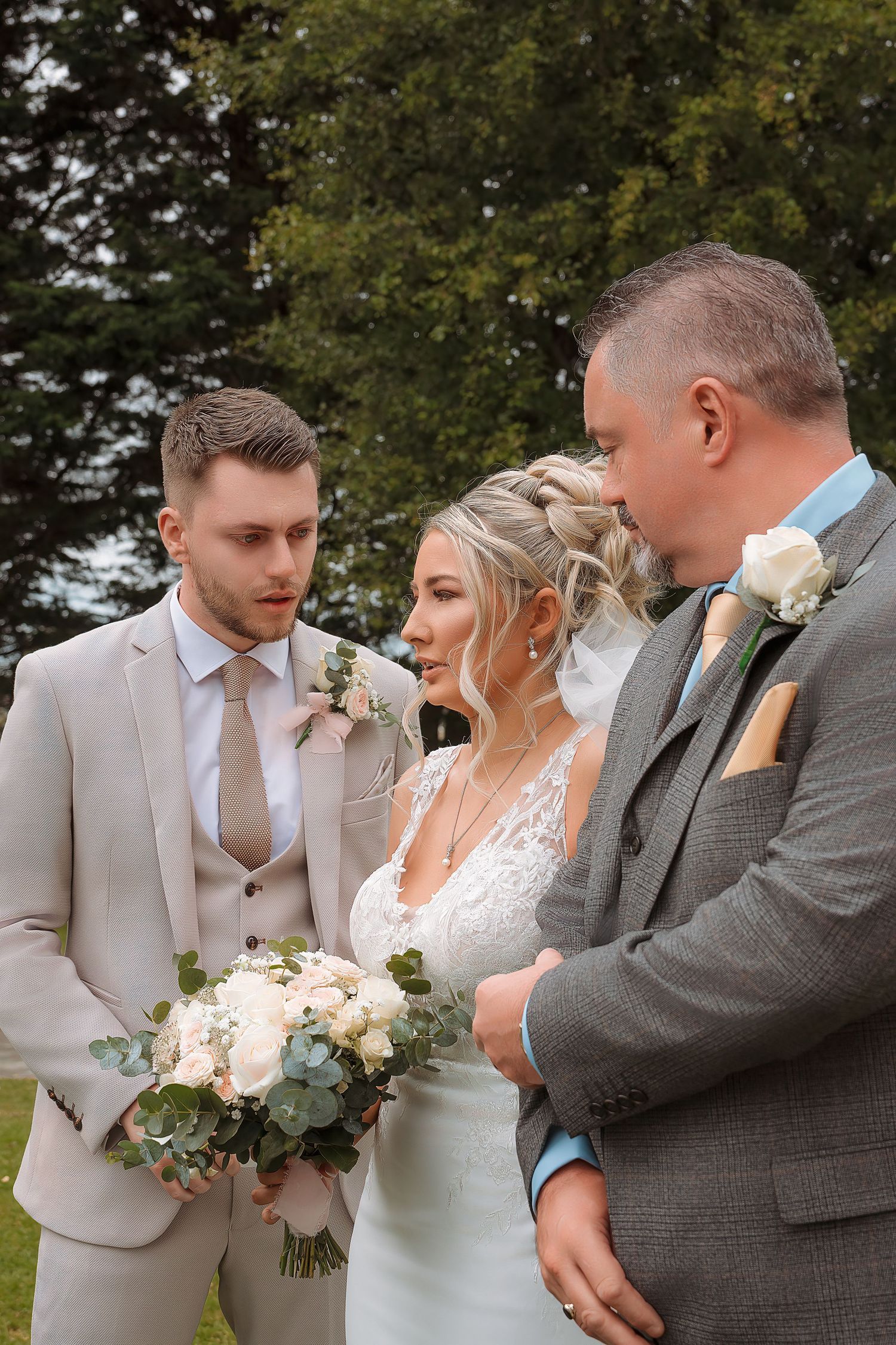 Bride and groom exchange vows outdoors with officiant, bride holding white rose bouquet, both in elegant wedding attire.