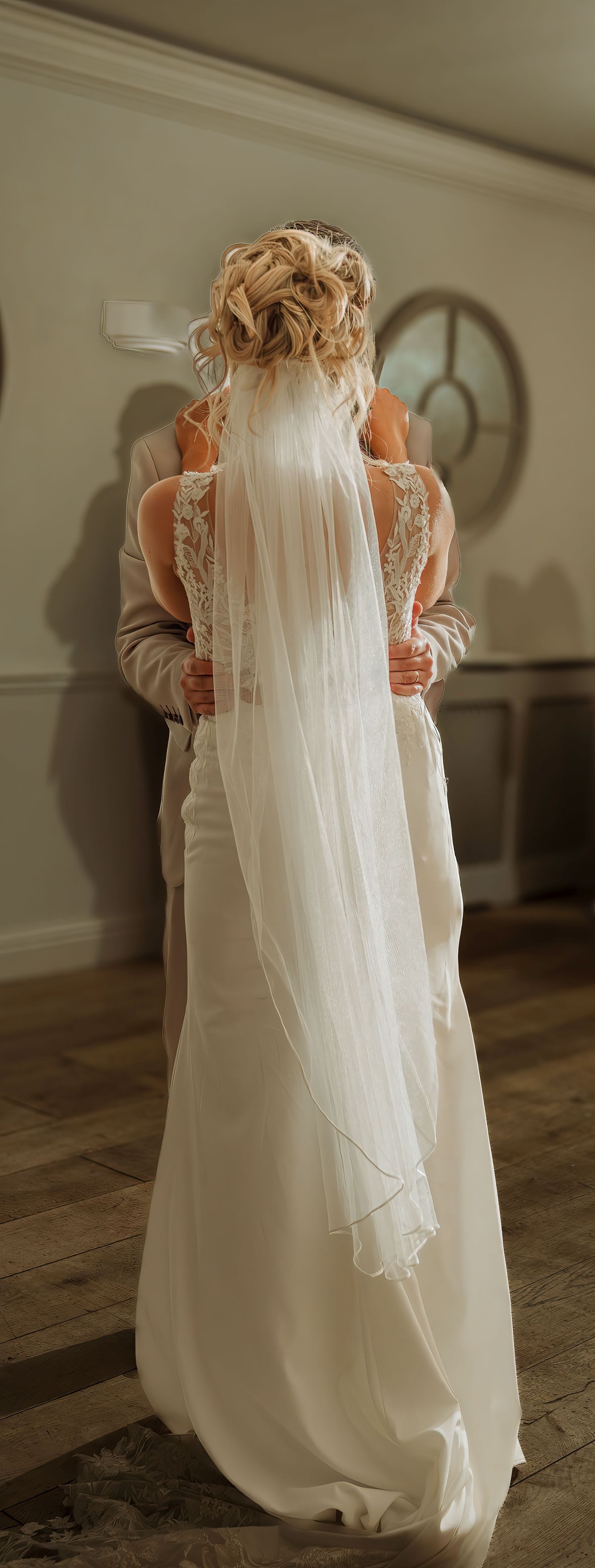 Bride in elegant white wedding gown with lace back detail and long flowing veil, viewed from behind.