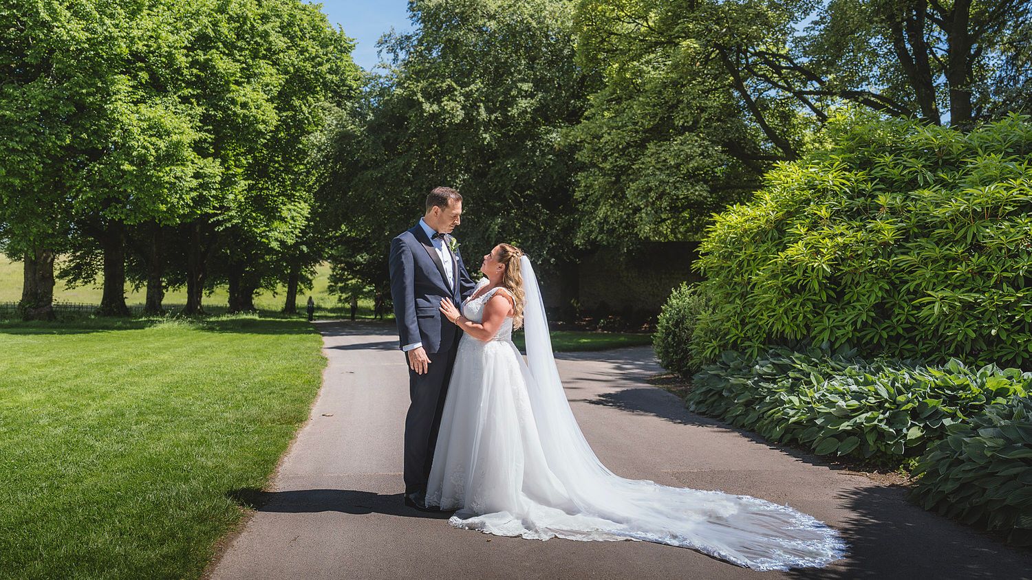 Bride and groom share a romantic moment on a garden path surrounded by lush green trees on their wedding day.
