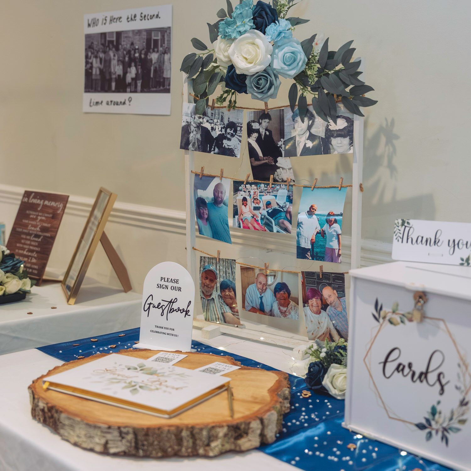 Wedding guest book table display with photos, cards box, blue floral decor, and wood slice centerpiece at elegant reception.