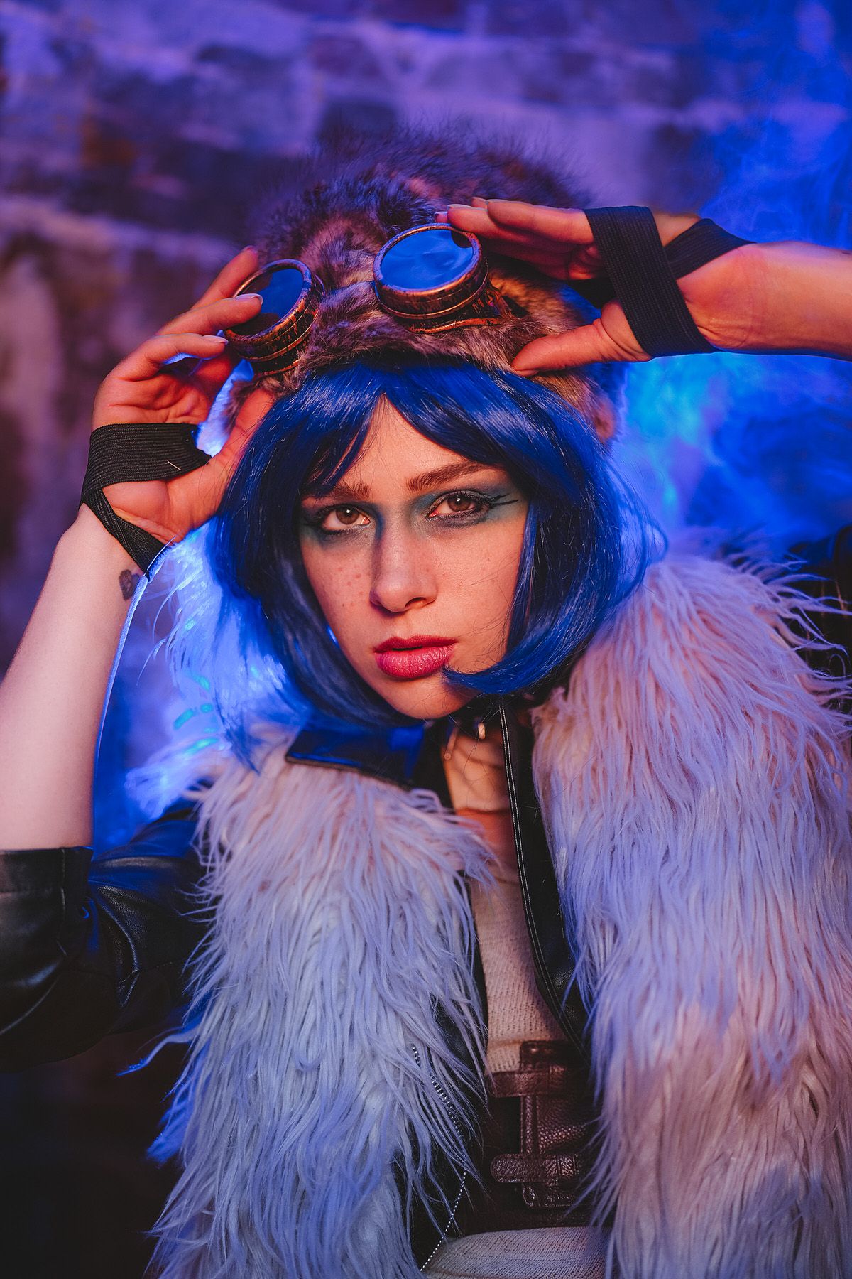 Woman with blue wig adjusting steampunk goggles wearing white fur coat with blue neon lighting.