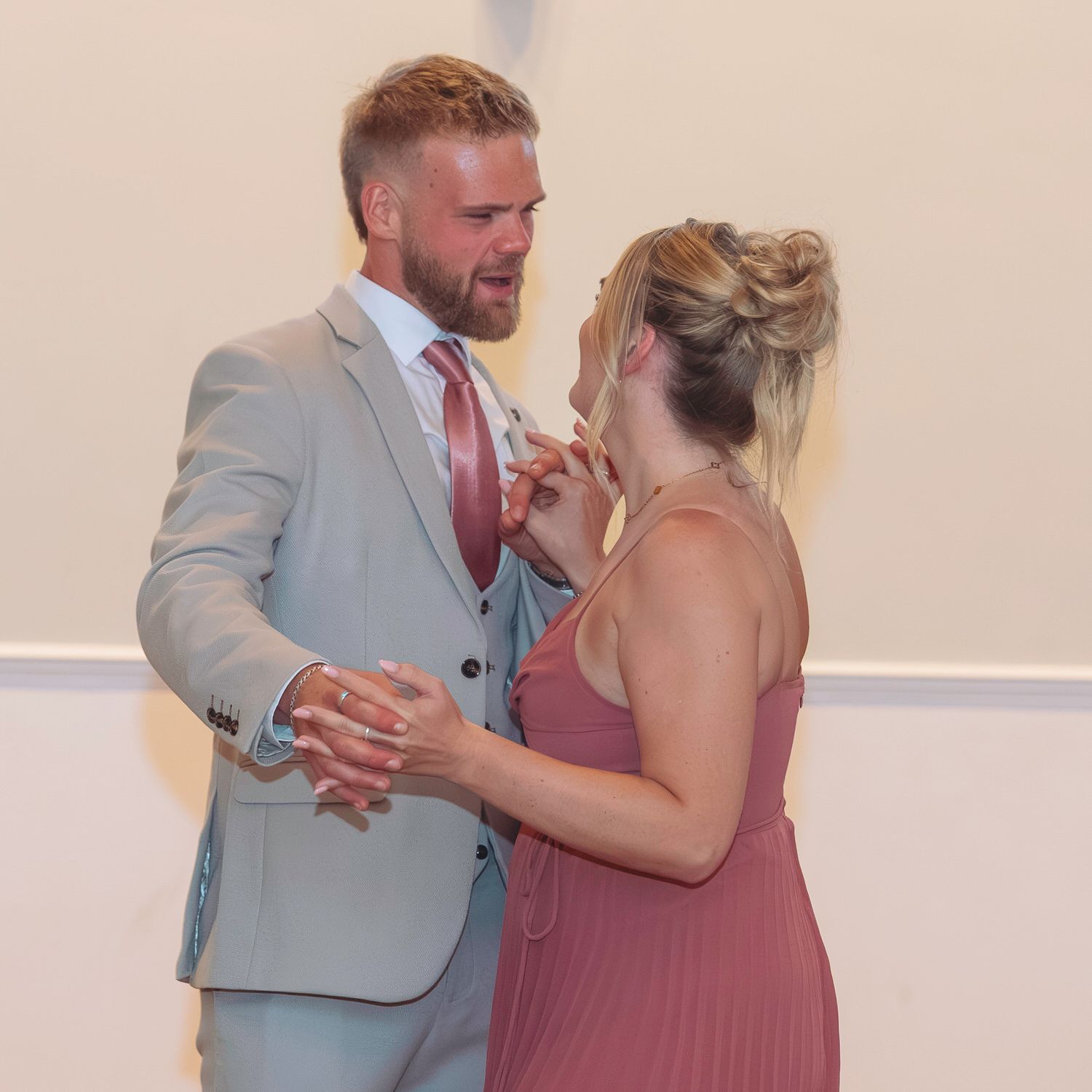 Couple in formal attire sharing a romantic moment, man in gray suit with pink tie, woman in dusty rose dress.