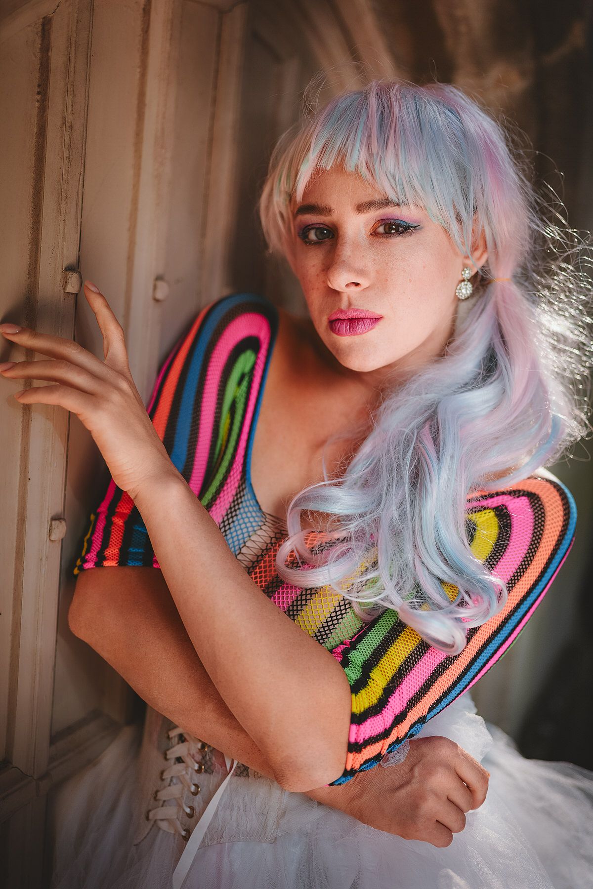 Woman with pastel blue and pink hair in vibrant striped colorful top and white tulle skirt posing.