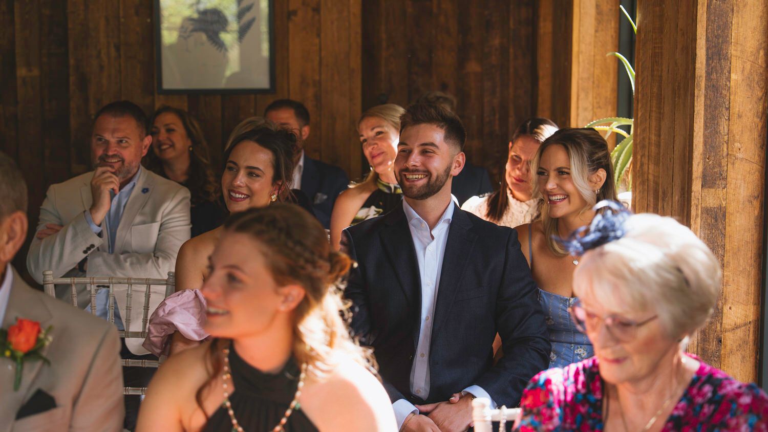 Wedding guests smiling and laughing during a ceremony inside a rustic barn venue.