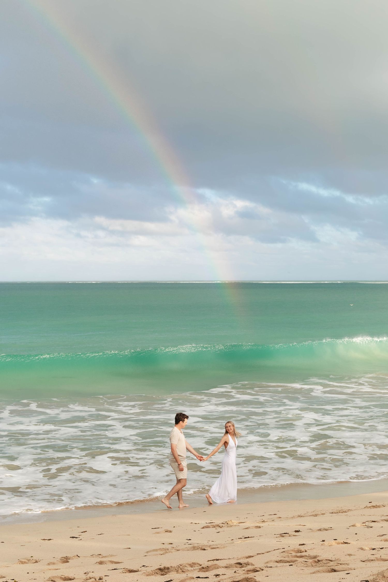 Fiji couples photographer capturing a romantic couple walking on a tropical beach beneath a rainbow in Fiji.