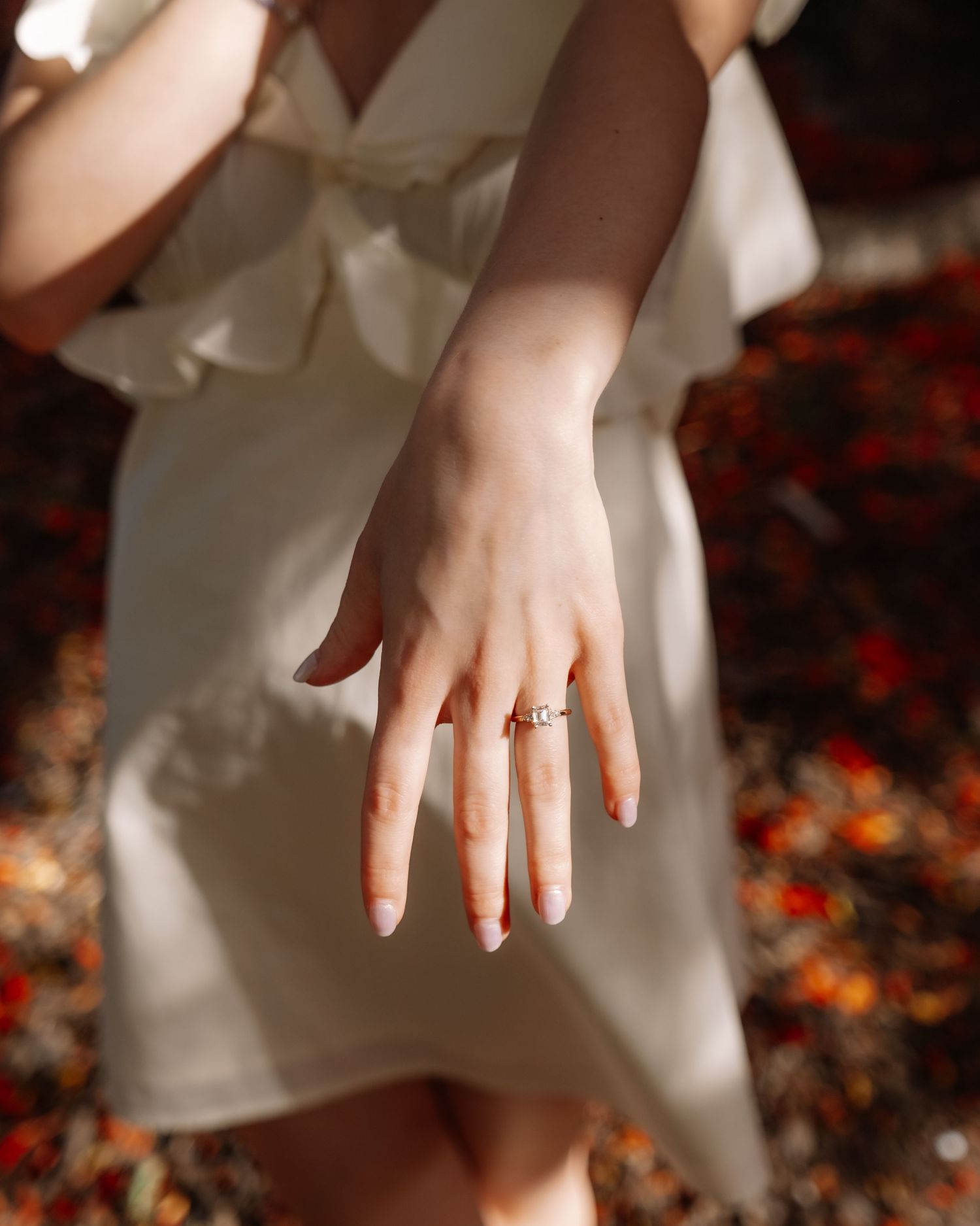 Close-up of an engagement ring on a woman's hand wearing a white ruffled dress.