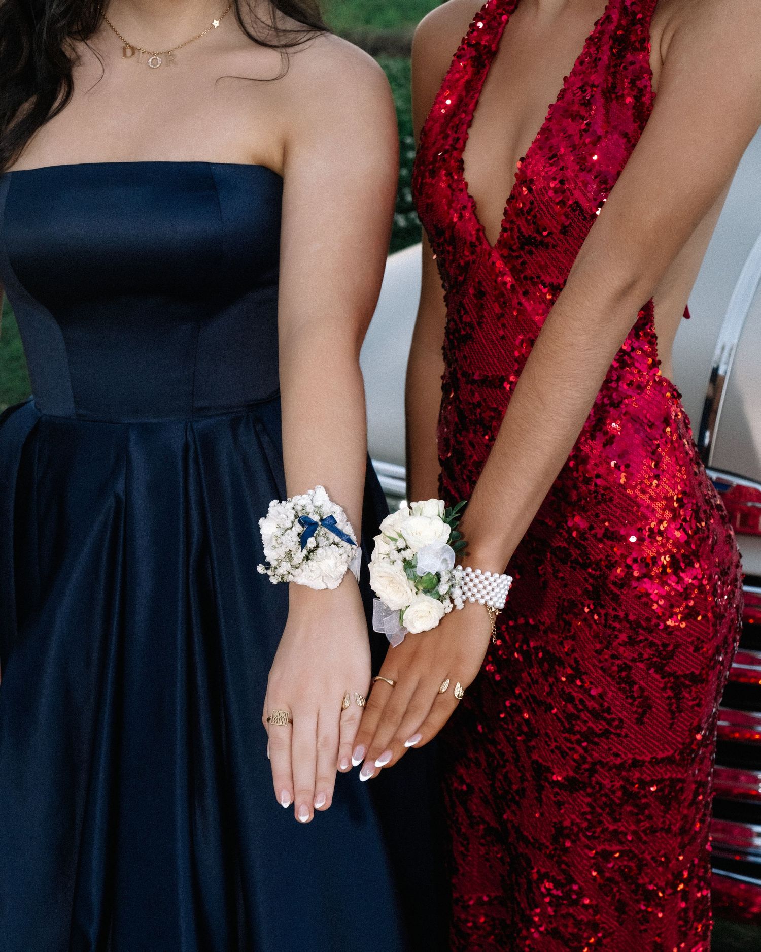 Two women in navy and red sequin formal gowns showing wrist corsages at prom.