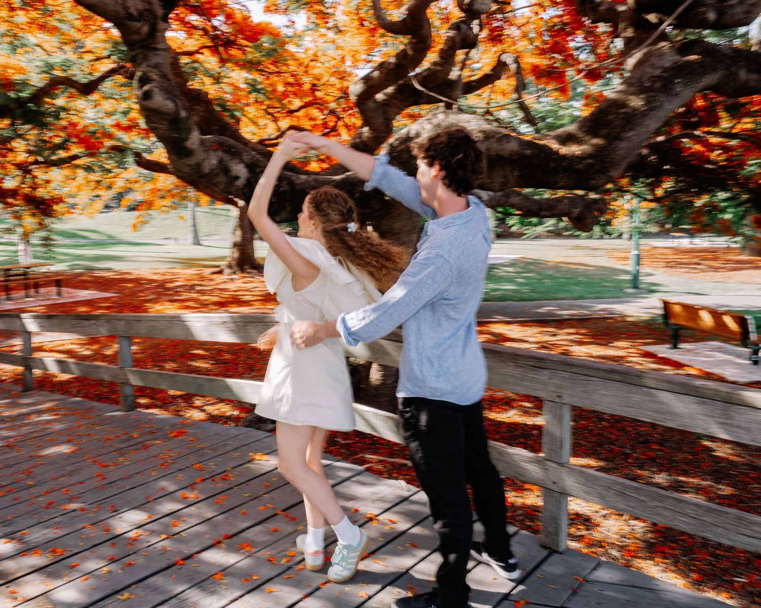 Couple dancing joyfully on a wooden bridge beneath a vibrant red flowering tree.