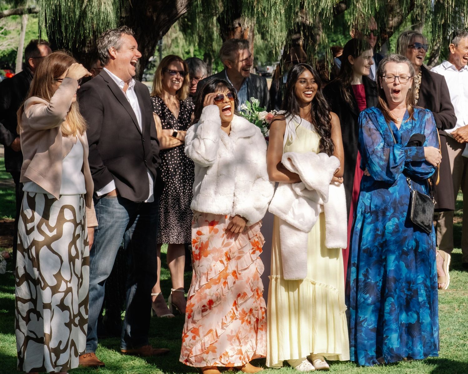 Joyful wedding guests laughing and celebrating outdoors at a garden ceremony.