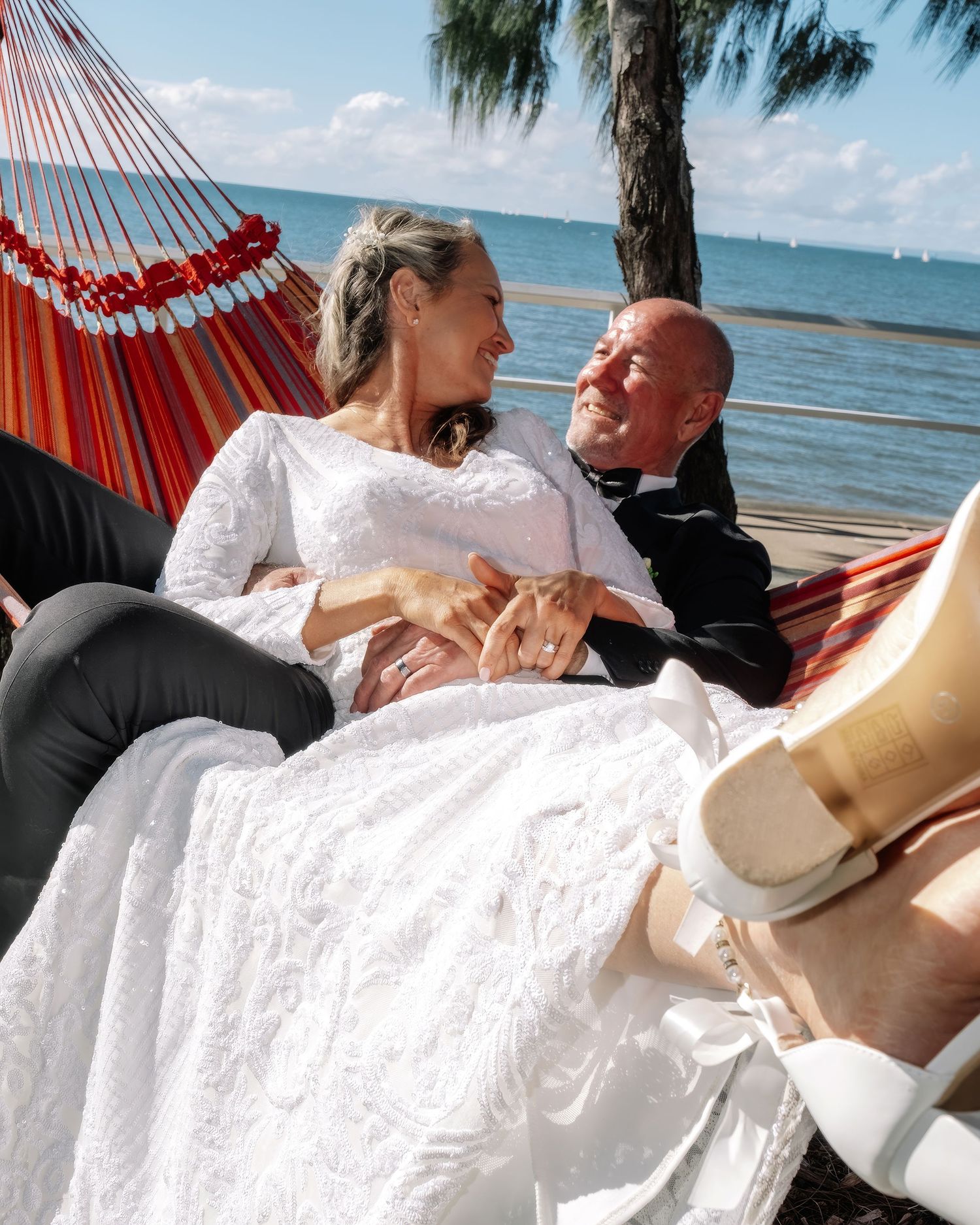 Bride and groom relaxing together in a colorful striped hammock by the ocean.