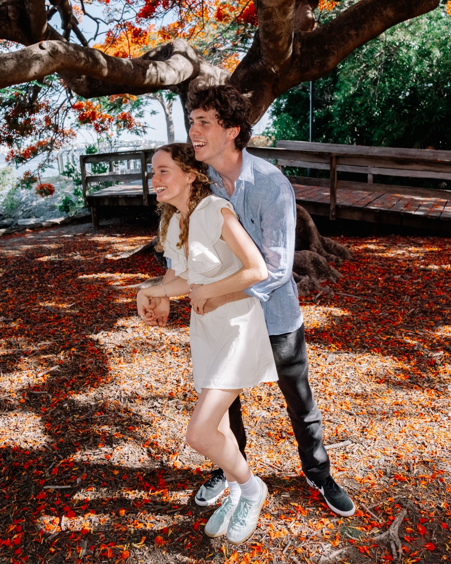 Engaged couple laughing and running hand in hand on a carpet of red fallen petals.