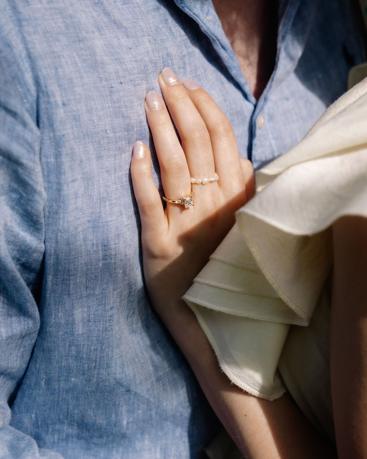 Close-up of an engagement ring on a woman's hand resting against a blue linen shirt.