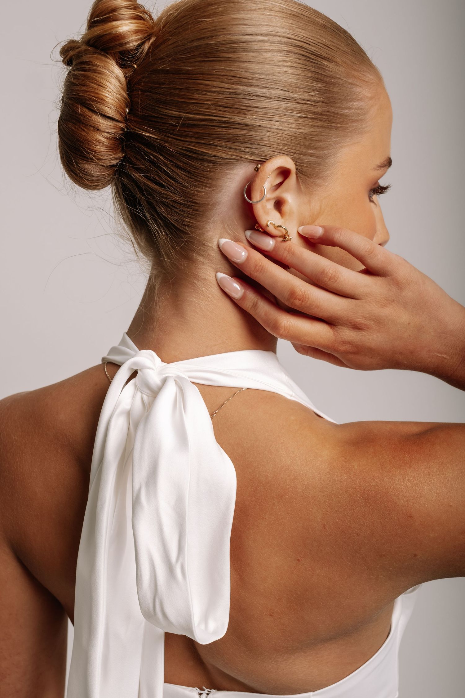 Back view of a woman with hair in a bun wearing a white halter dress with gold ear cuff.