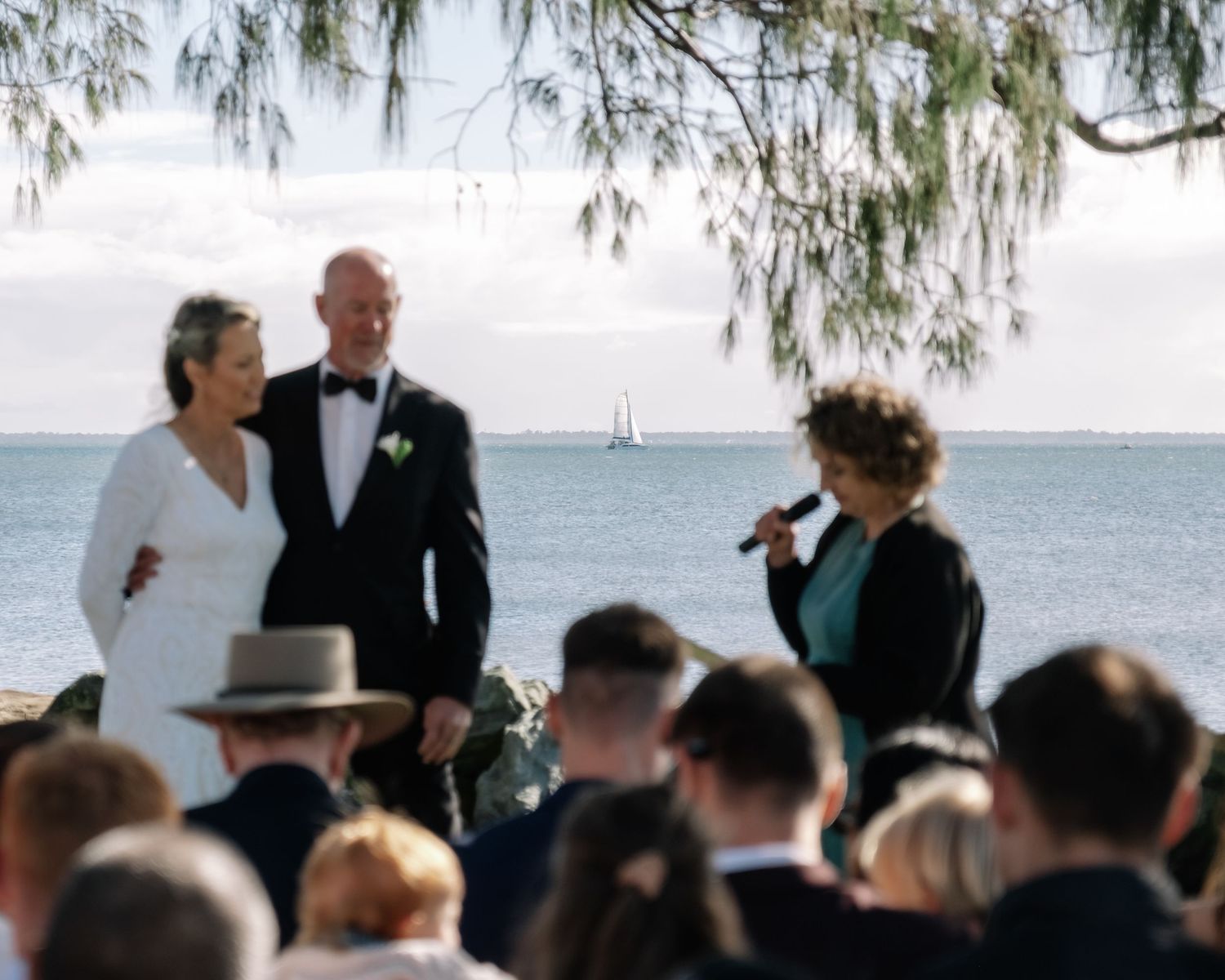 Outdoor beach wedding ceremony with couple exchanging vows before seated guests by the sea.