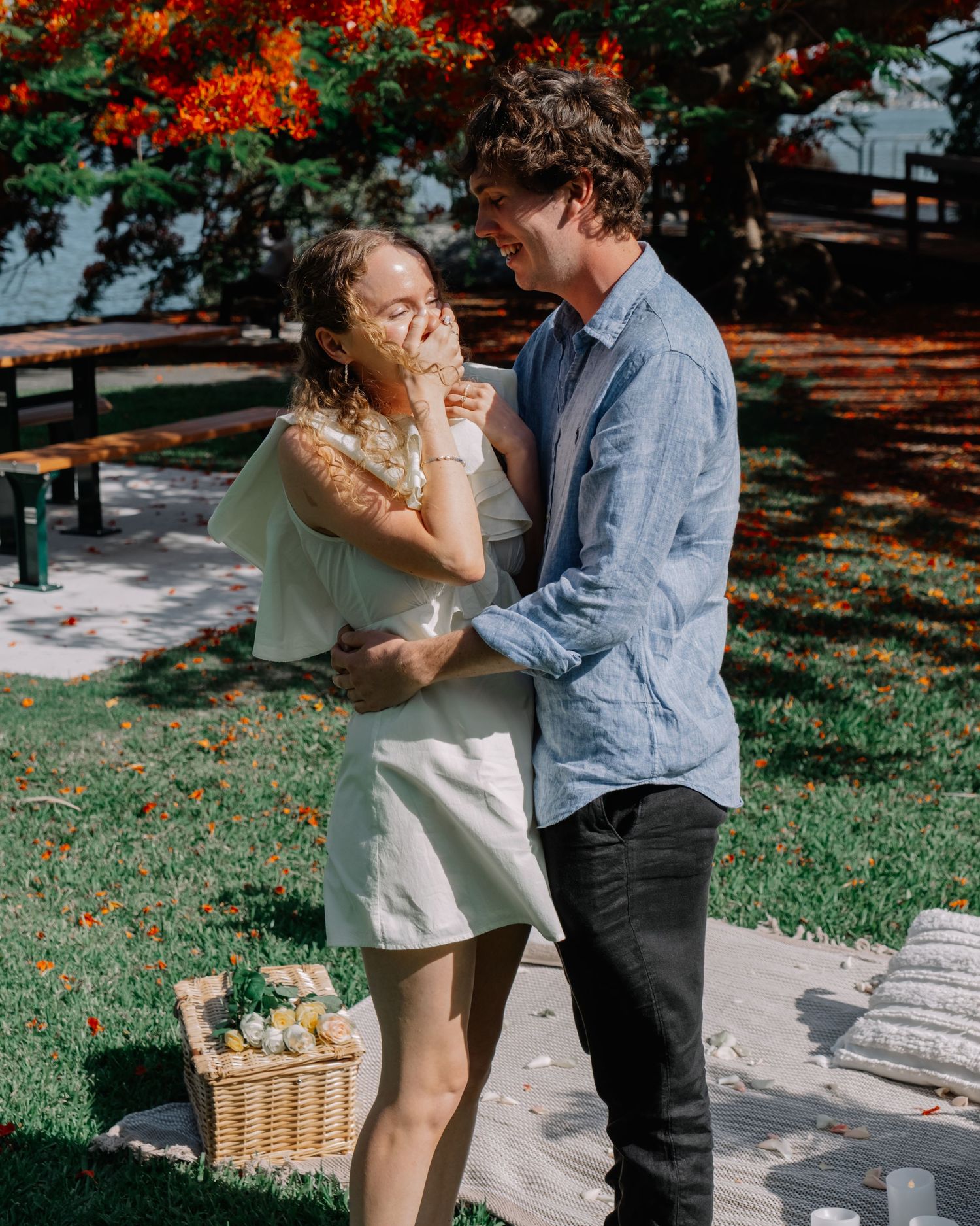 Happy couple sharing a tender moment beside a picnic basket under a red flowering tree.