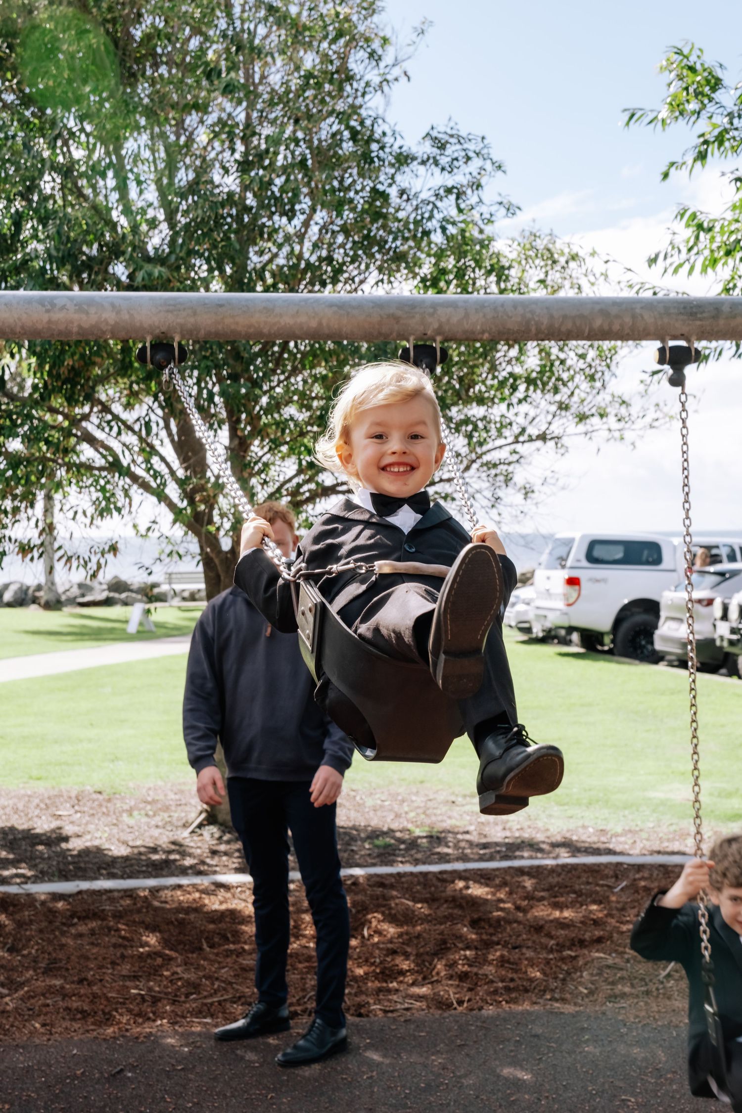 Happy toddler in a suit swinging at a playground during a wedding celebration.