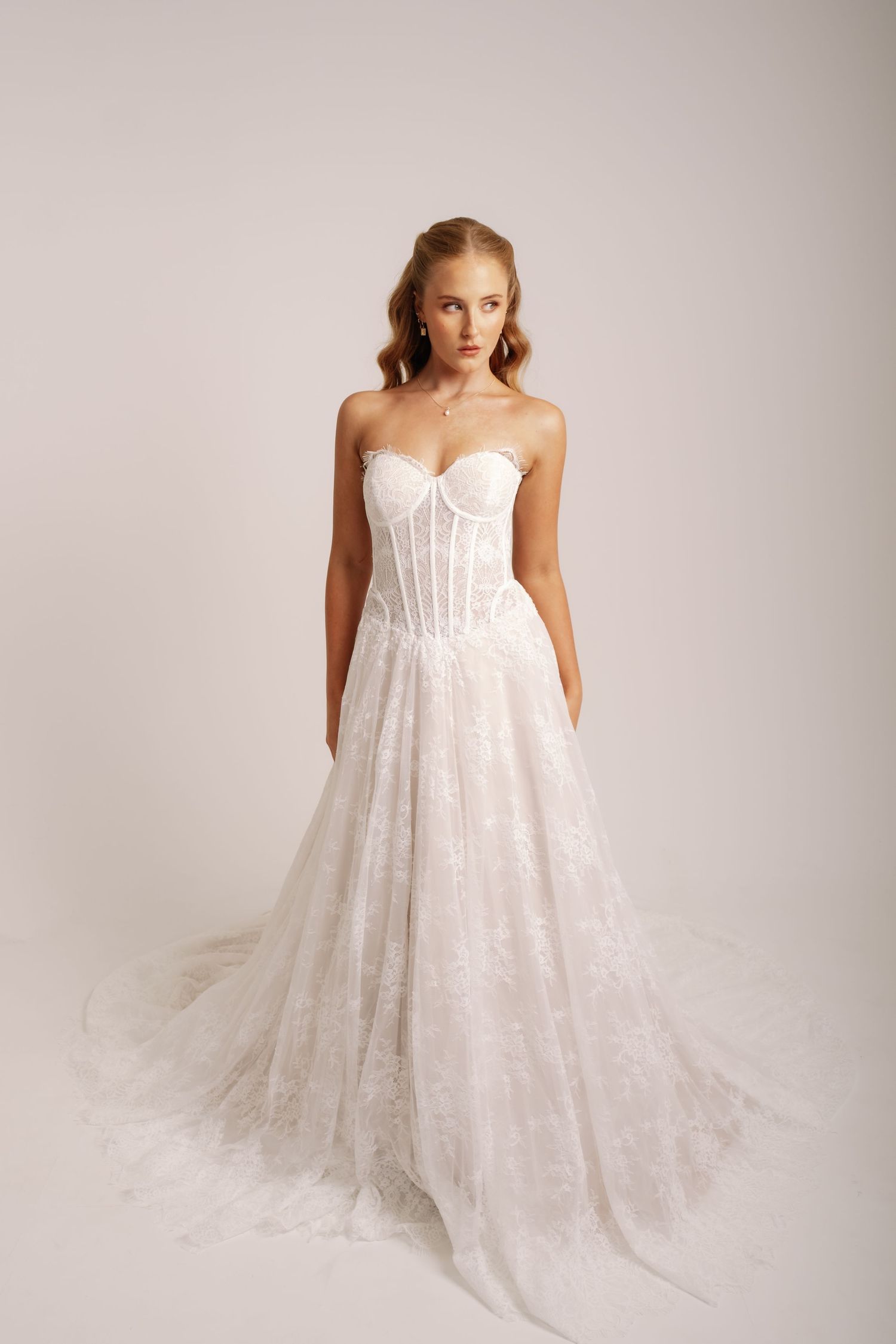 Elegant bride wearing a strapless white lace corset ballgown wedding dress in a studio setting.