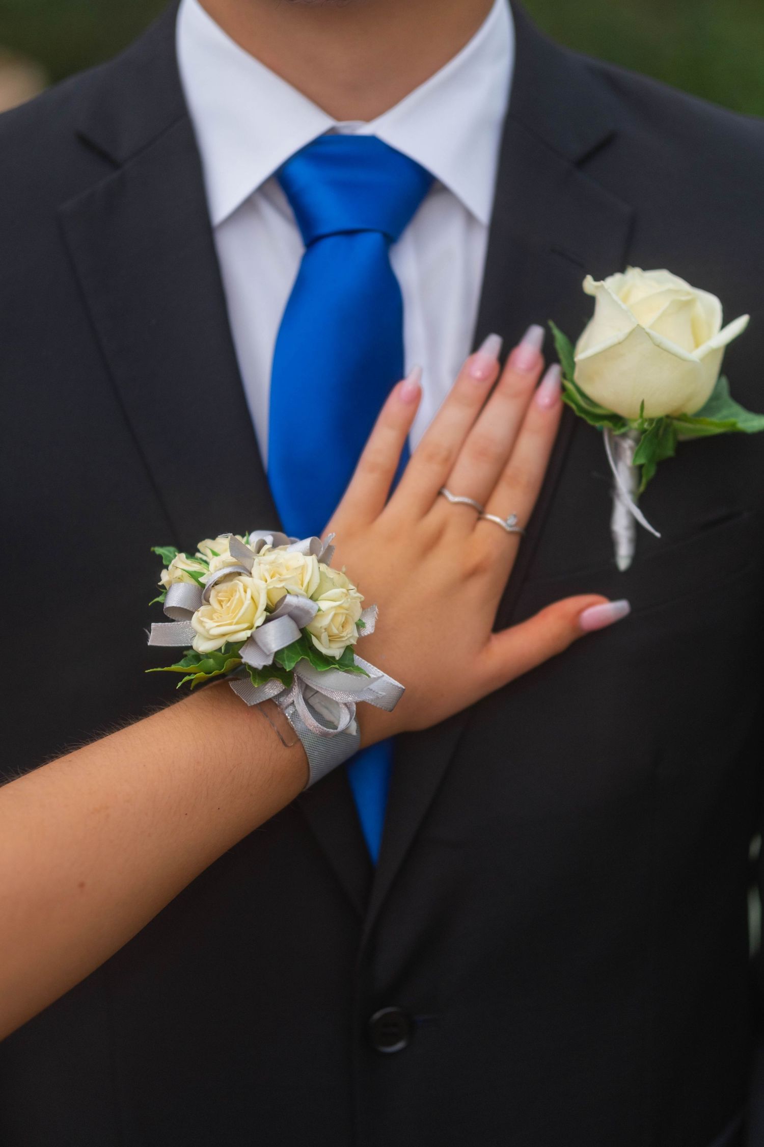 Close-up of prom corsage on wrist and boutonniere on black suit with blue tie.