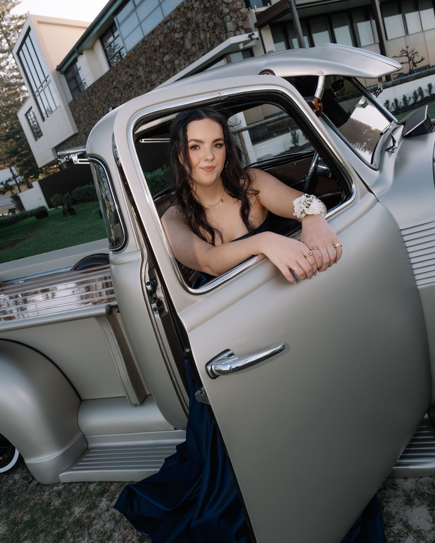 Young woman in a navy ballgown posing in the window of a vintage silver car.
