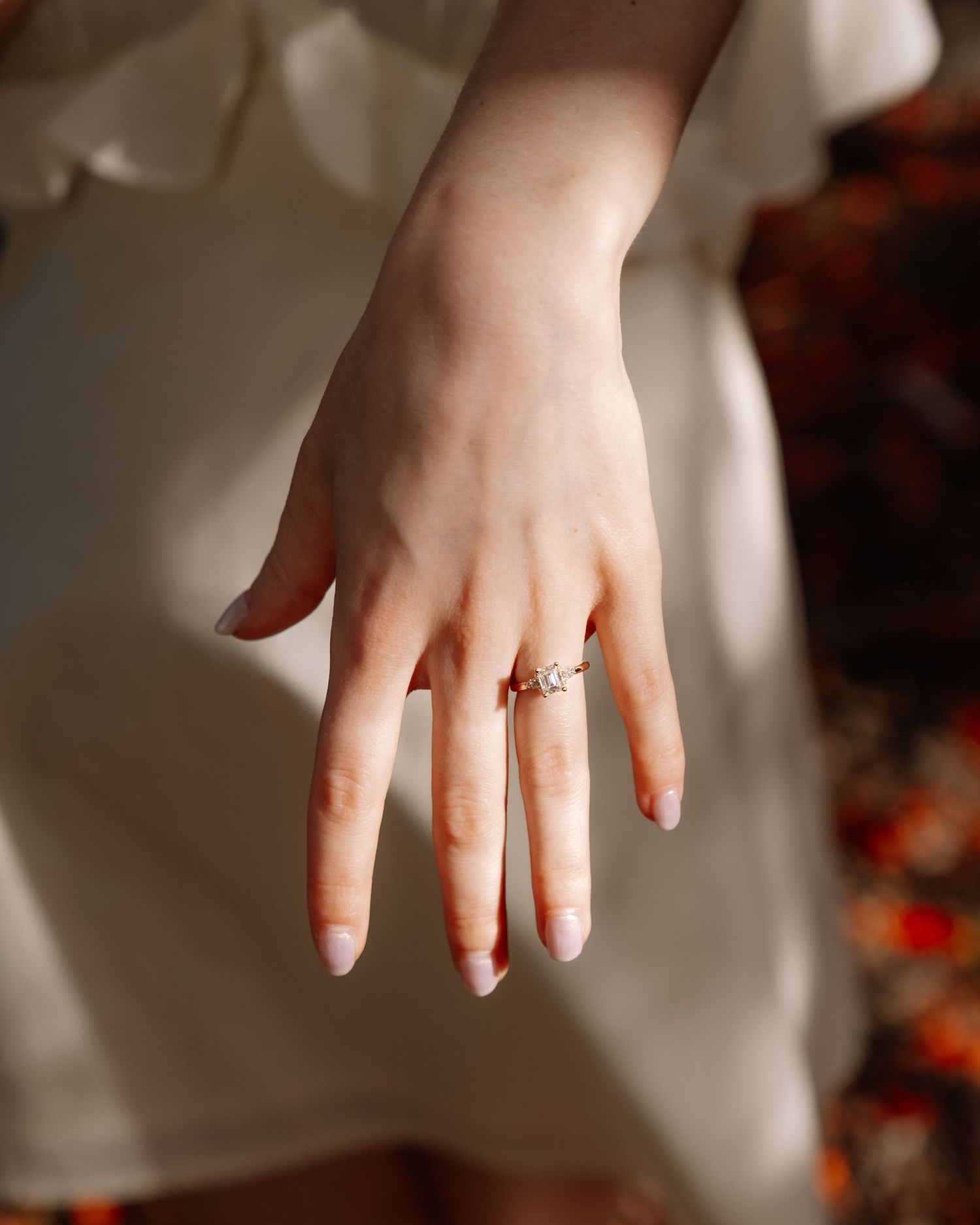 Close-up of elegant diamond engagement ring on bride's hand in white dress.
