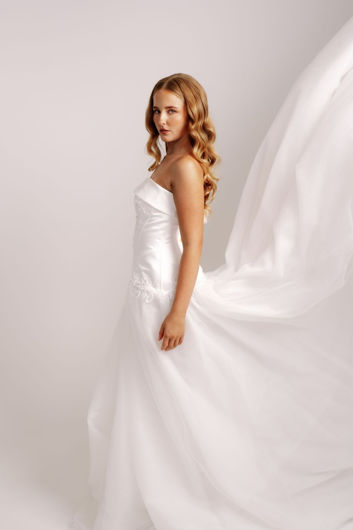 Beautiful bride in a flowing white strapless satin wedding gown with dramatic fabric movement.