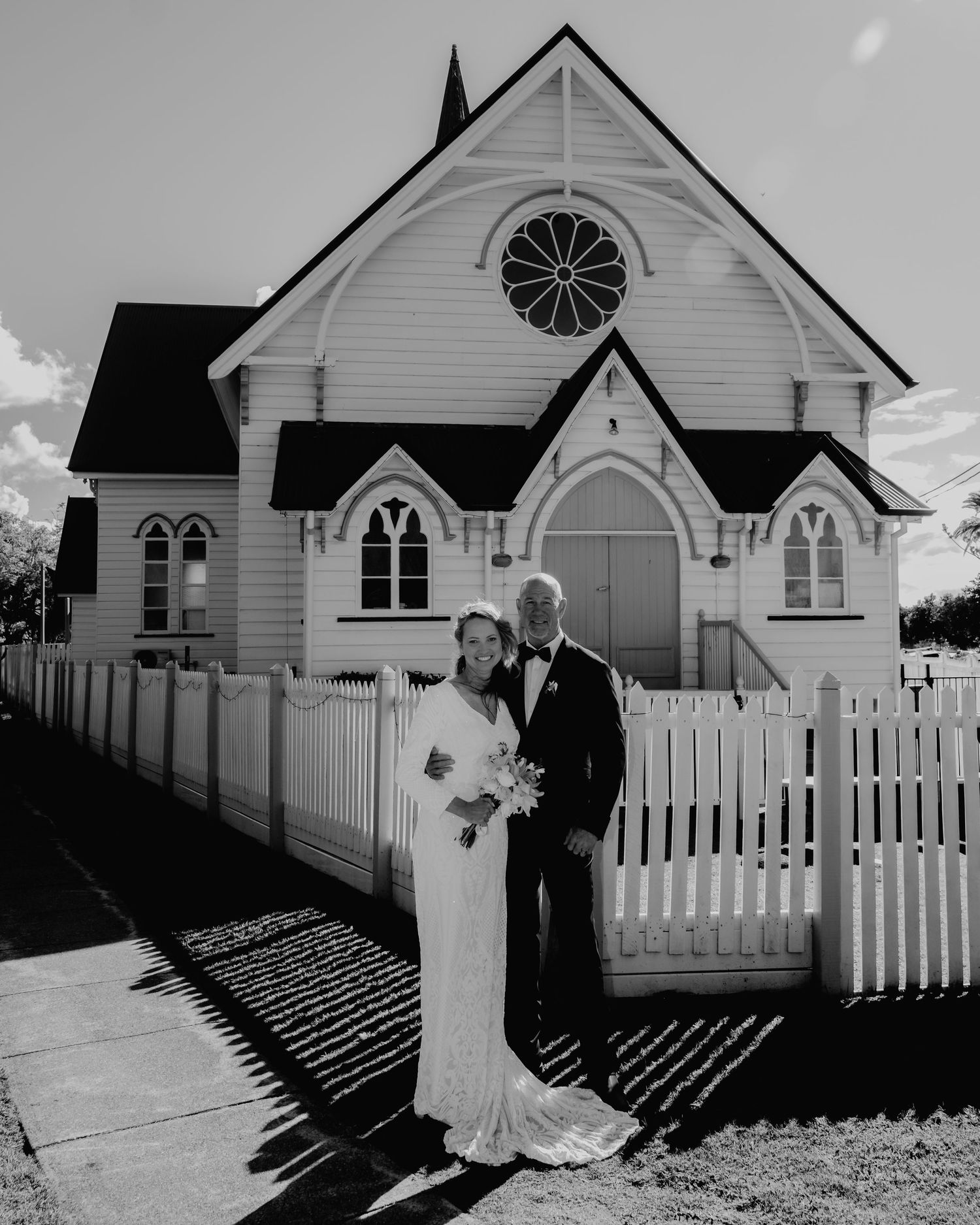 Bride and groom posing in black and white before a white wooden chapel.