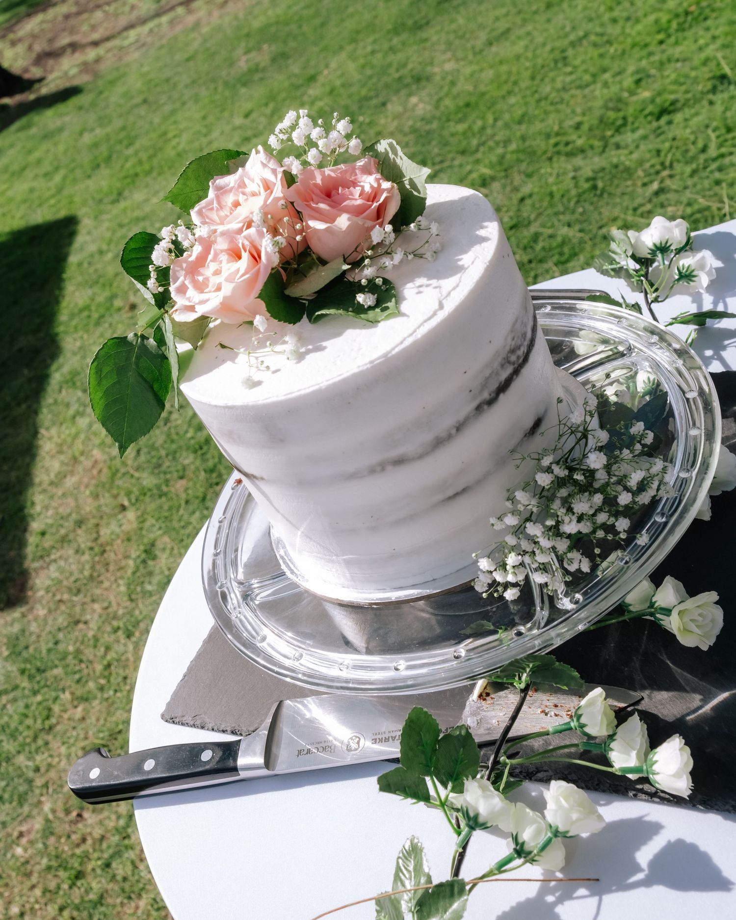 Elegant single-tier white wedding cake topped with pink roses and baby's breath flowers.
