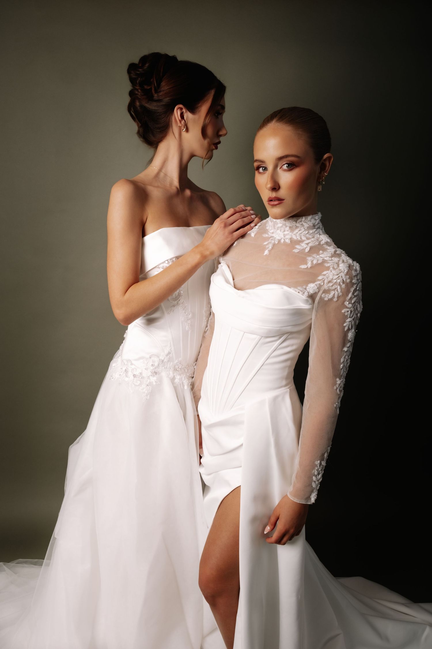 Two brides in stunning white wedding gowns posing together in a professional studio portrait shoot.