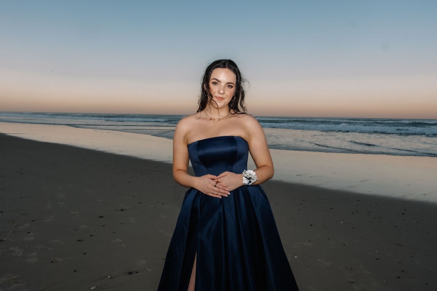 Woman wearing a strapless navy blue satin ballgown on a beach at sunset.