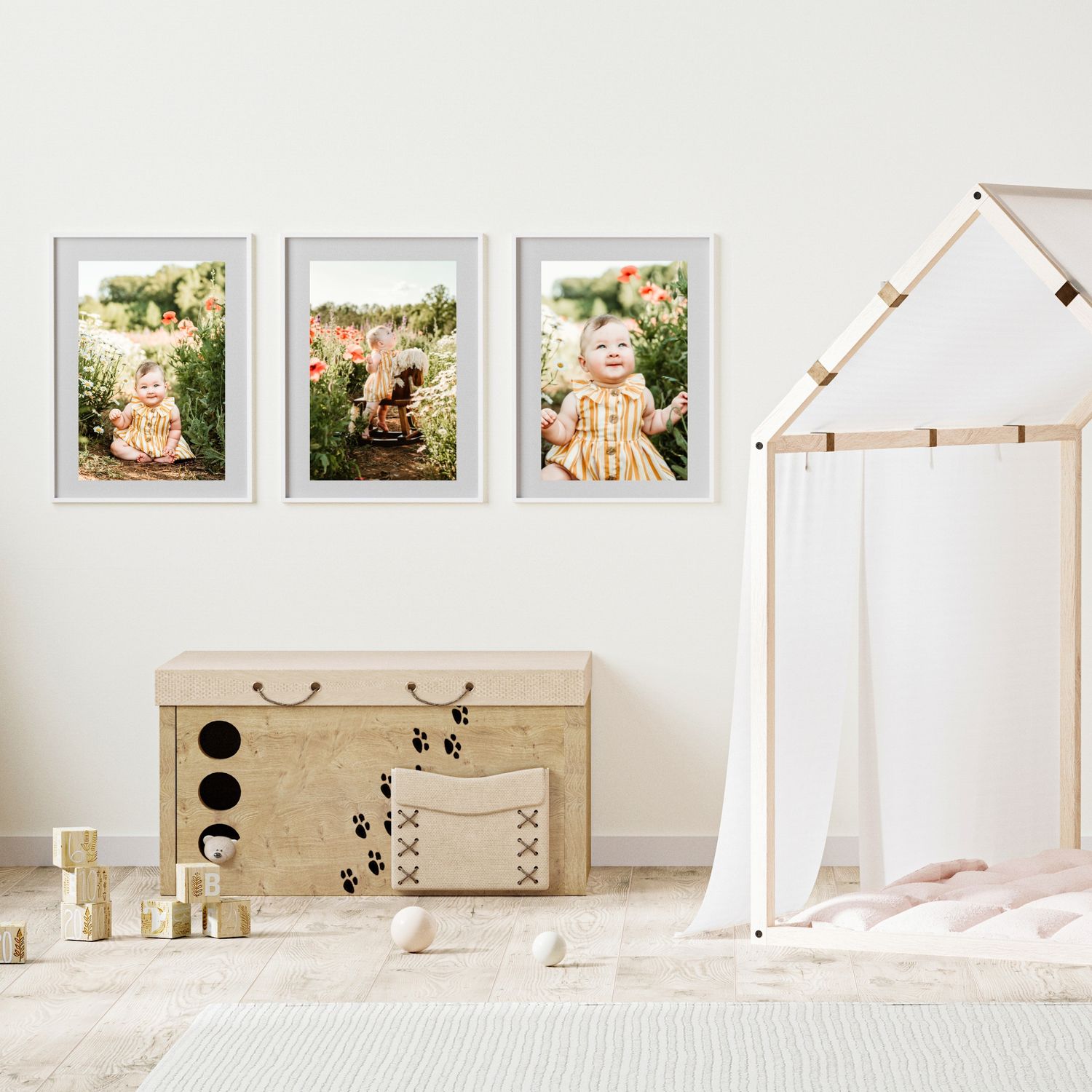 Three framed photos of a baby girl in a flower garden displayed on a nursery wall above a toy chest.
