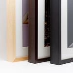 Three wooden picture frames in natural, espresso brown and black finishes lined up to show their depth and white mat borders.