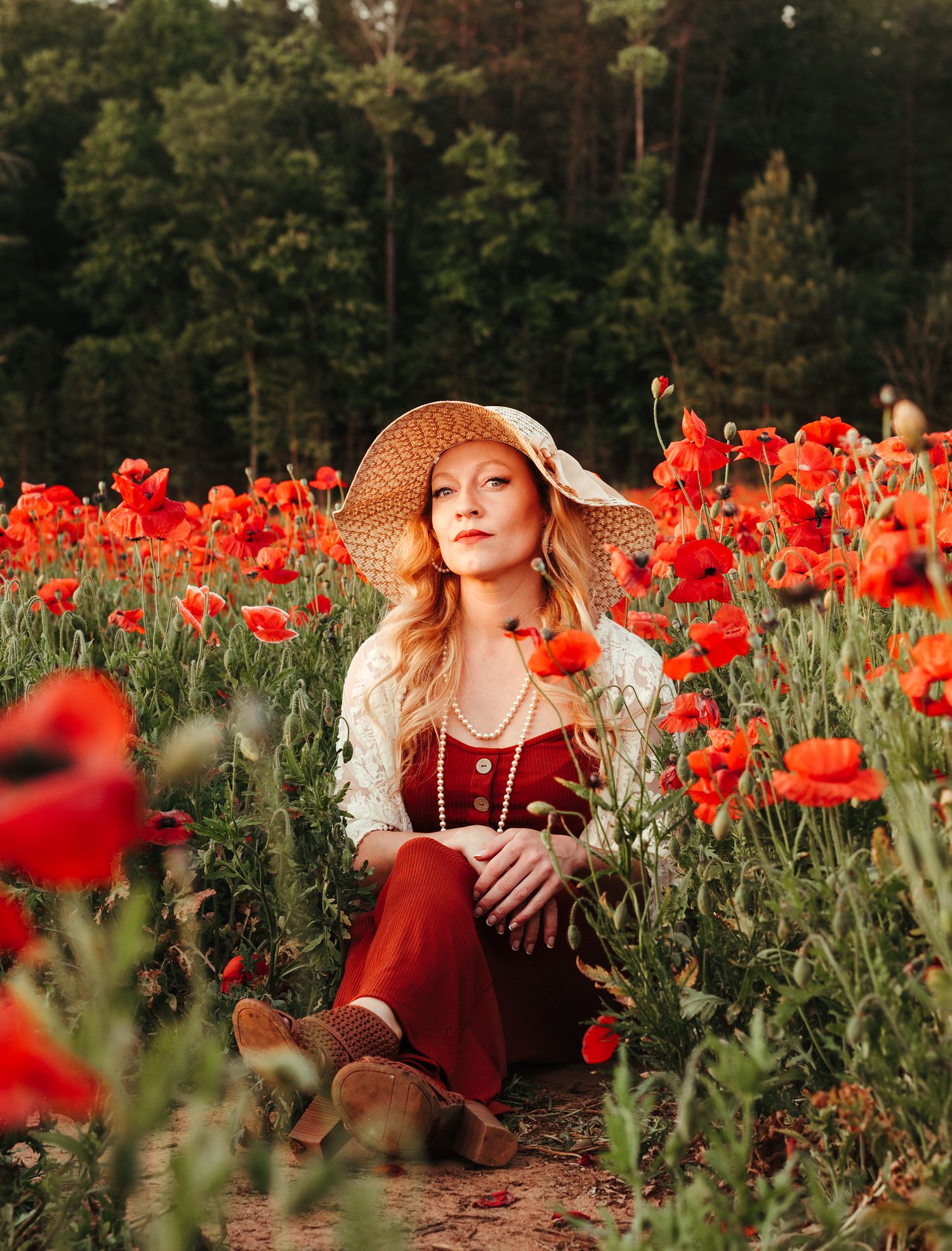 Blonde woman in straw hat sitting in a vibrant red poppy field.