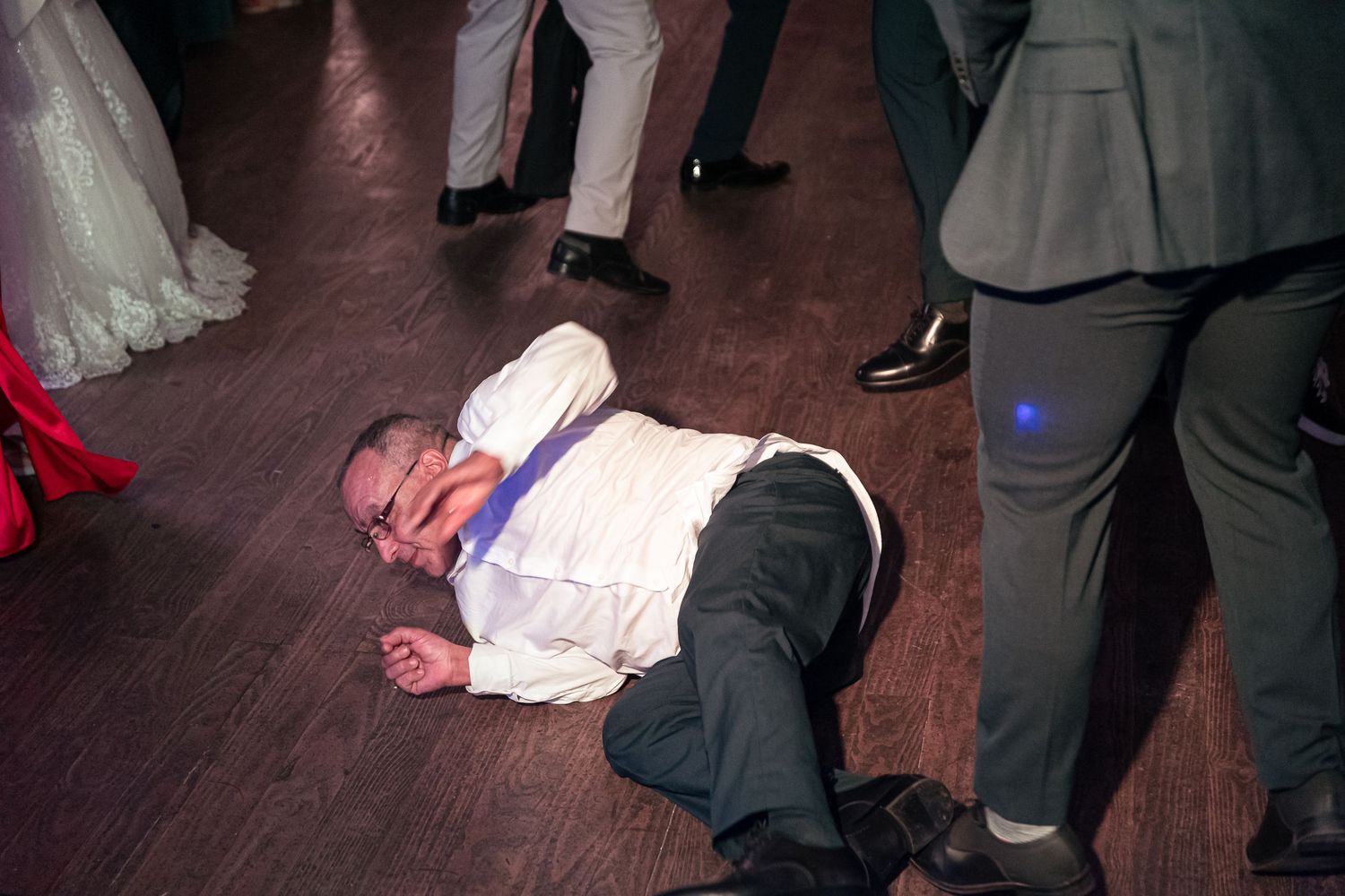 Wedding guests dance on a dark wooden dance floor during reception celebrations.