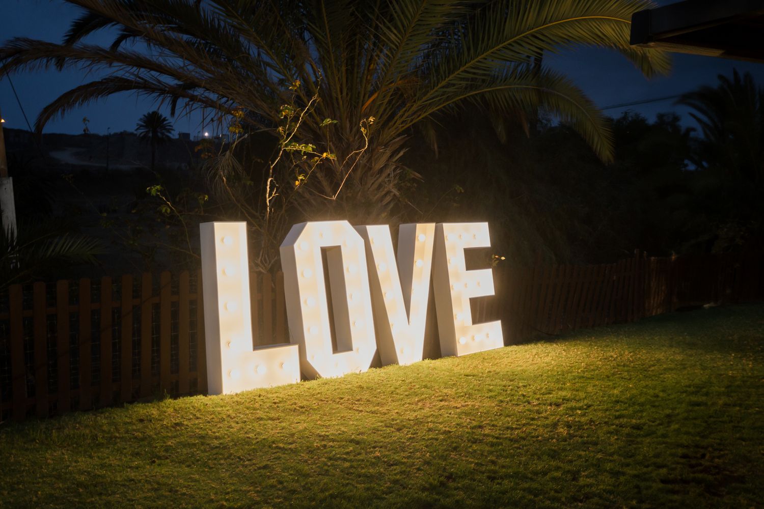 Large illuminated LOVE letters create a romantic backdrop on a grassy lawn at dusk.