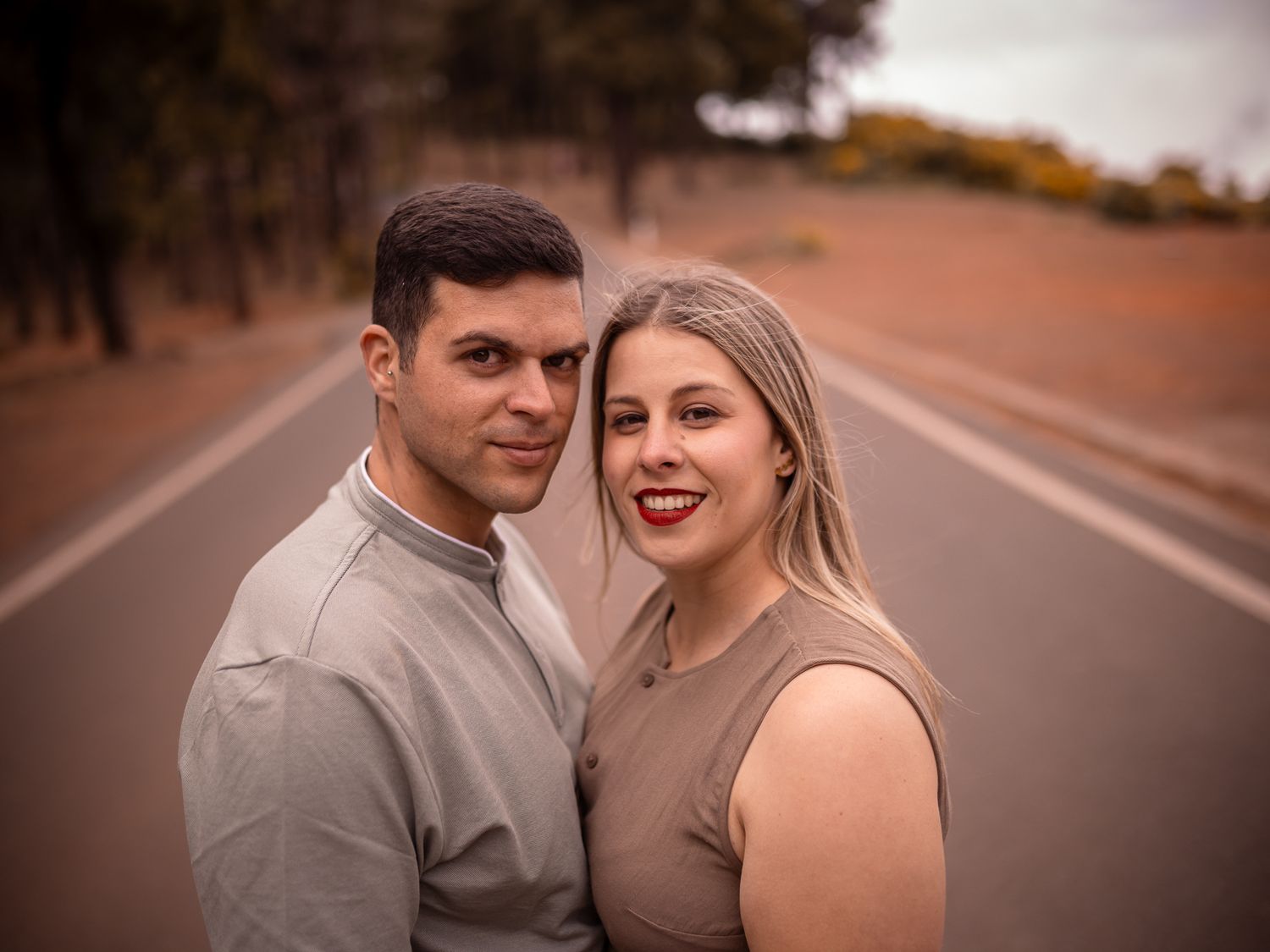 A romantic couple poses together on a paved road surrounded by nature.