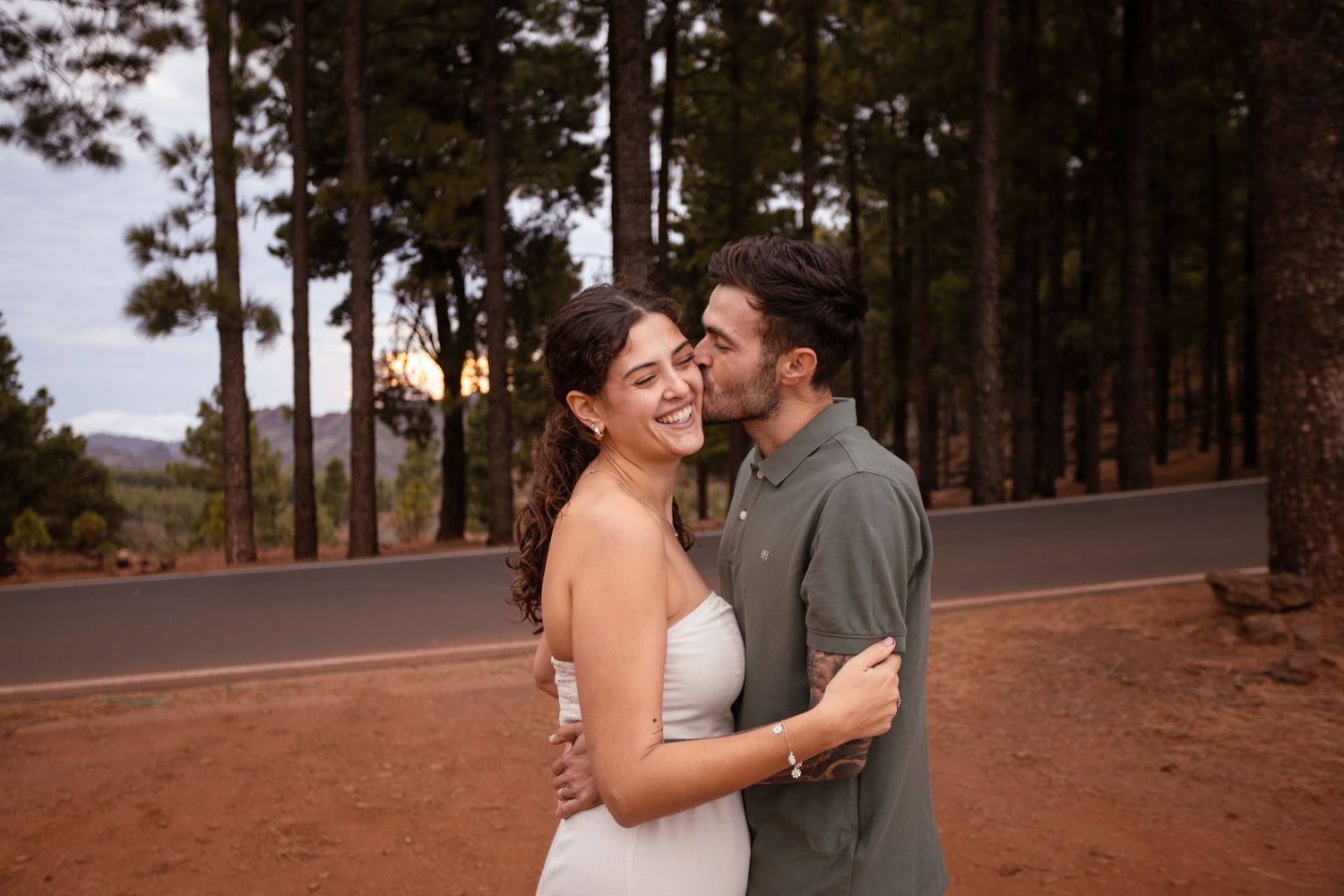 A couple embraces on a tree-lined path during sunset, creating a romantic silhouette against the natural backdrop.