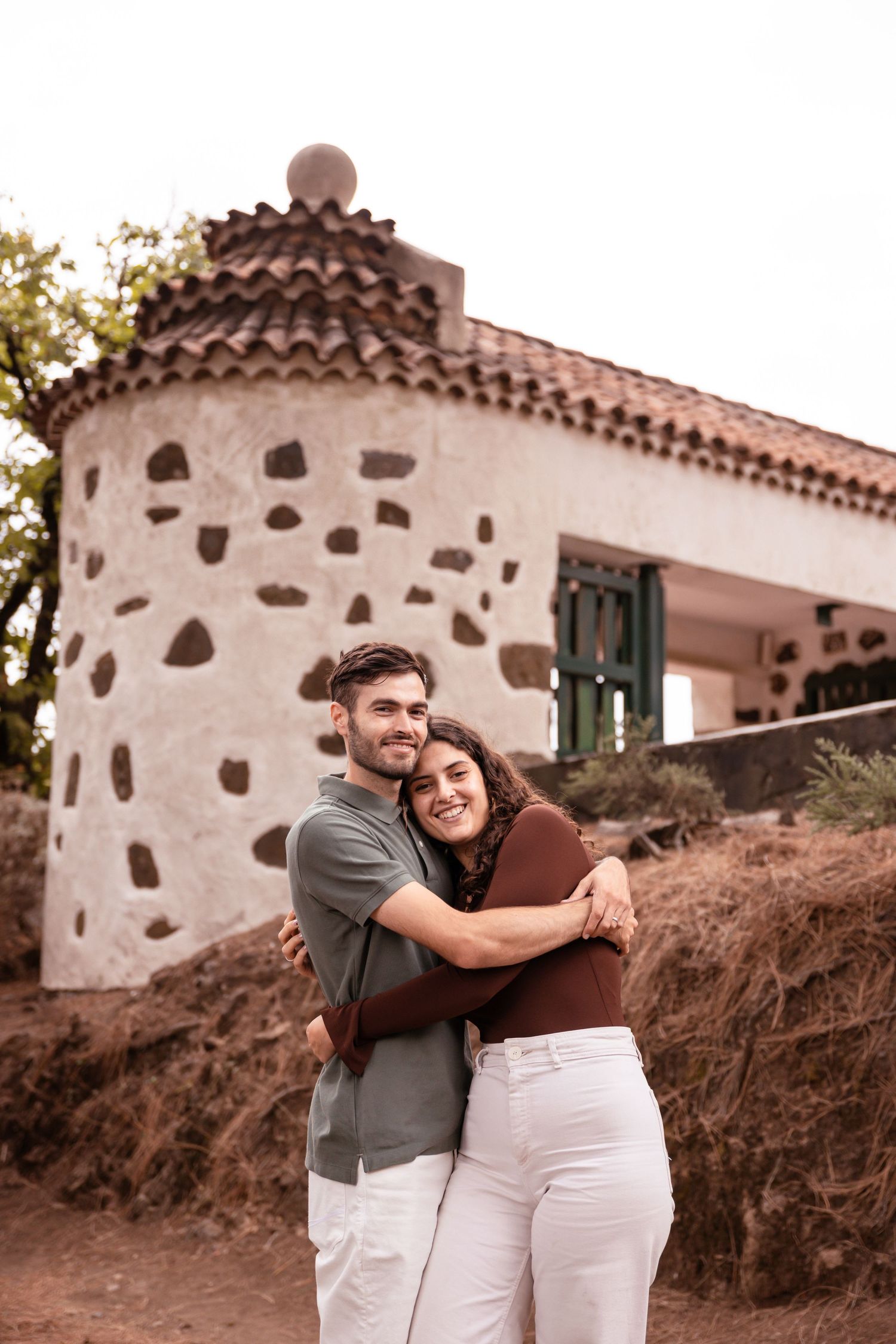 Couple hugging in front of a traditional stone building with Spanish architecture.