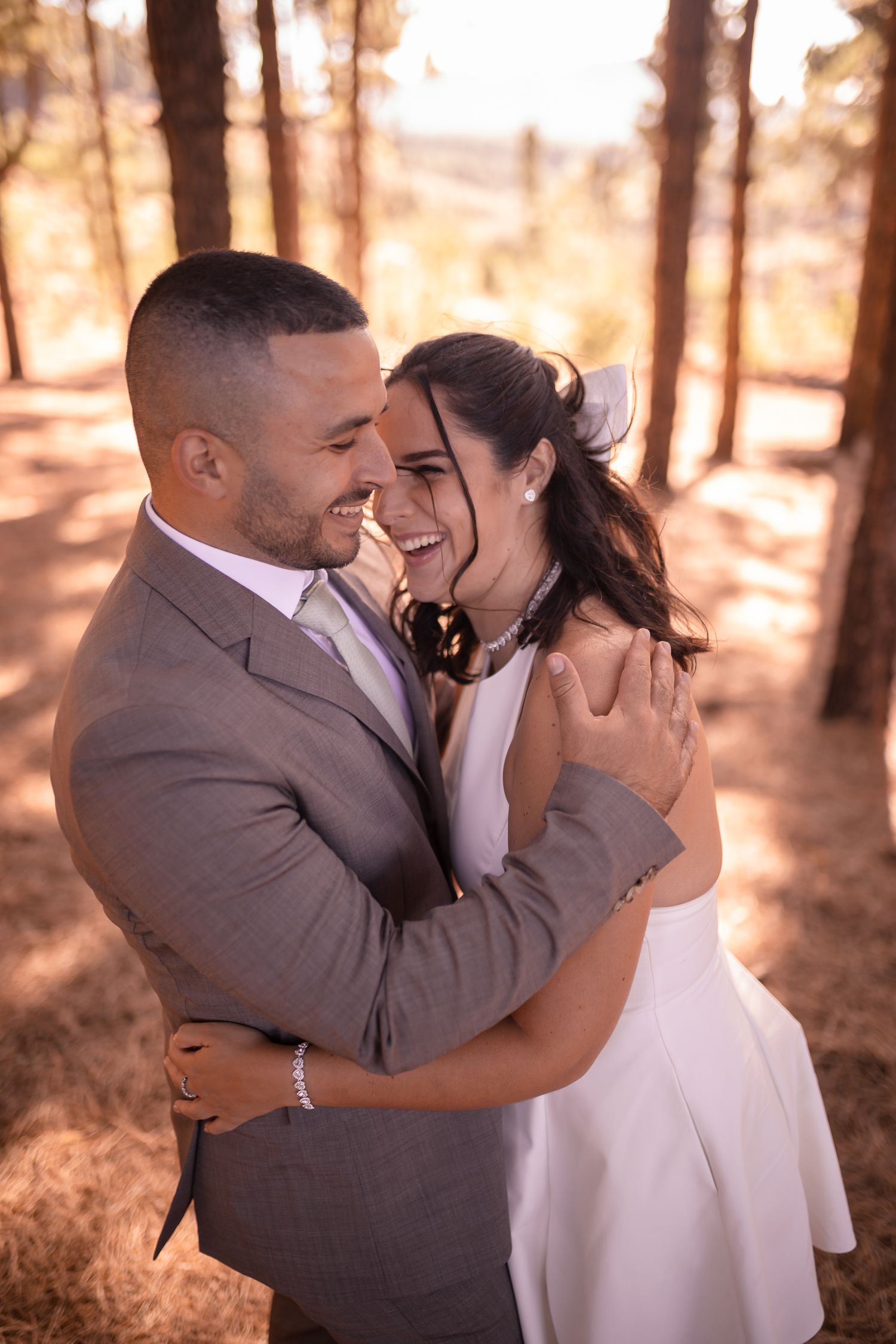 A couple shares tender moments in a sunlit forest setting wearing formal wedding attire.