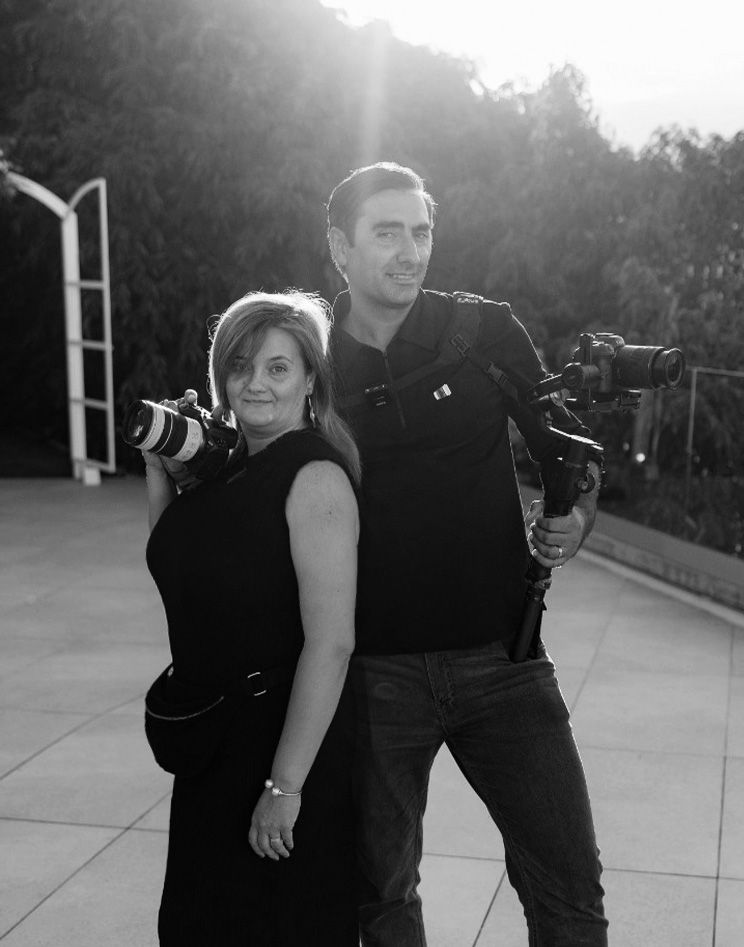 Professional photographers in black attire work together during an outdoor photoshoot in natural lighting.