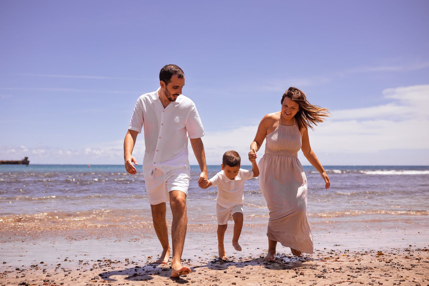 Family walking together holding hands along the shoreline on a sunny beach day.